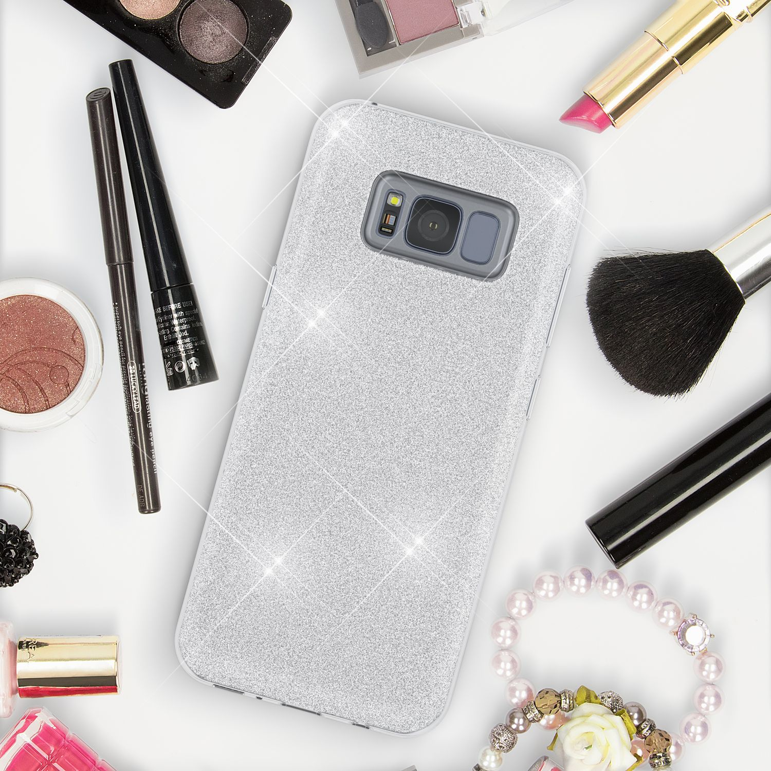 Glitzernde Handyhülle umgeben von Make-up-Artikeln.