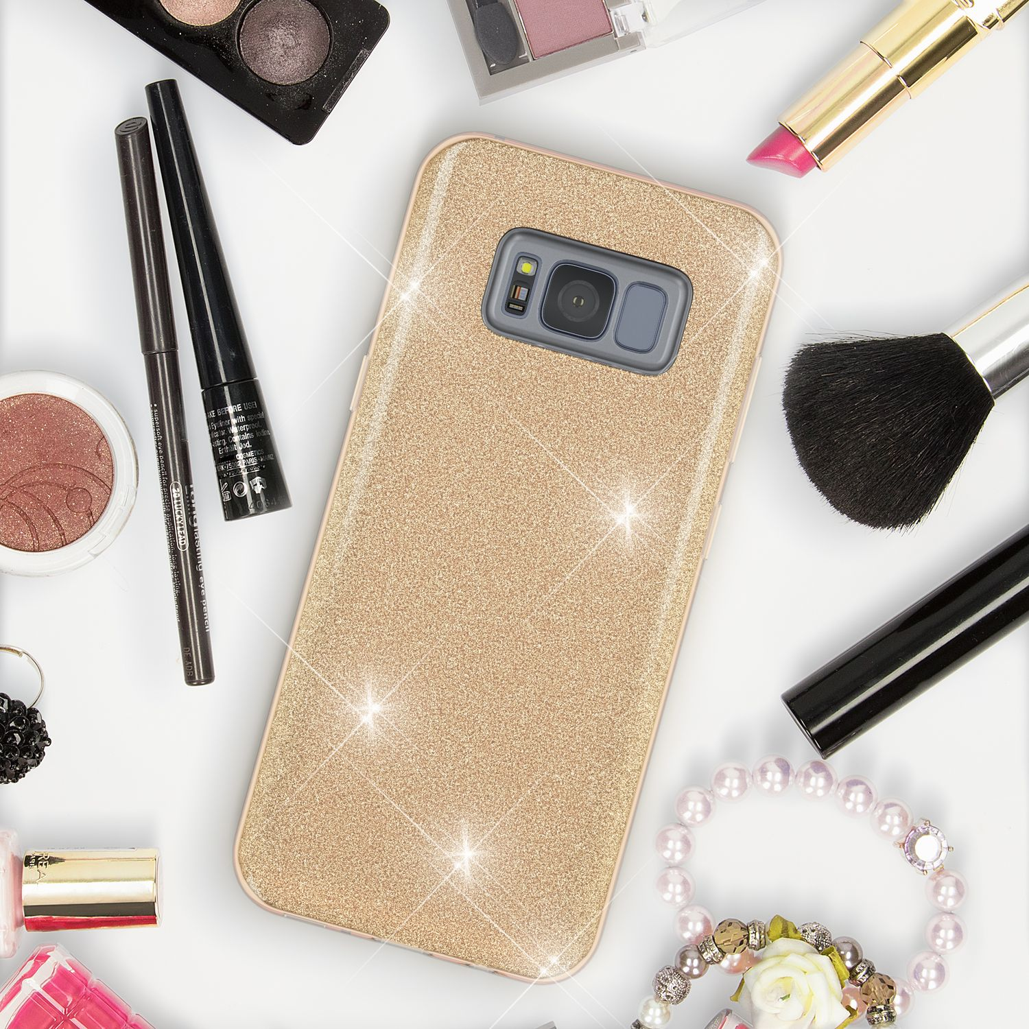 Goldener, glitzernder Handyhülle umgeben von Kosmetika wie Lippenstift und Pinsel.