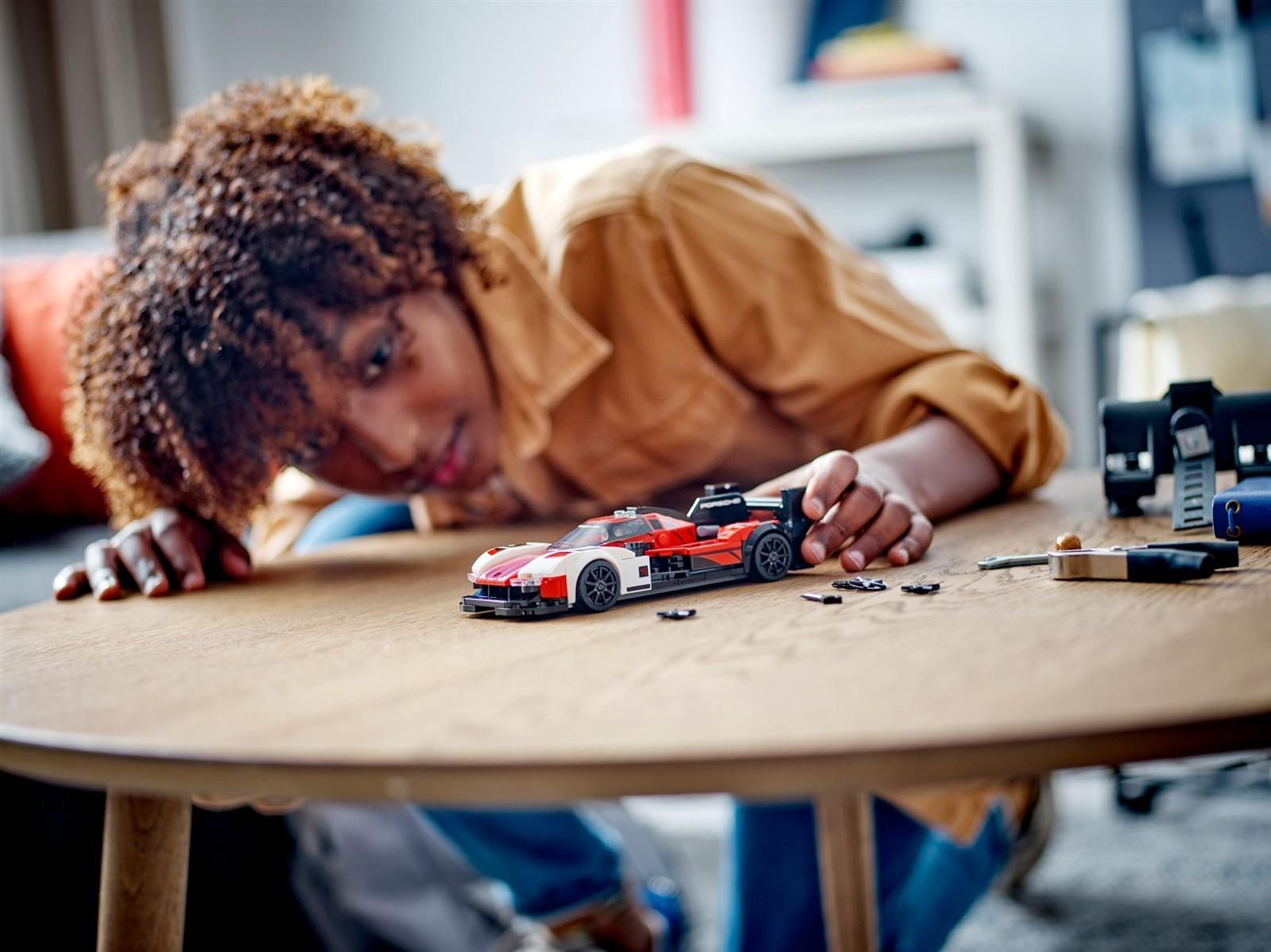 Eine Person beugt sich über einen Holztisch und konzentriert sich auf einen rot-weißen Lego-Rennwagen.