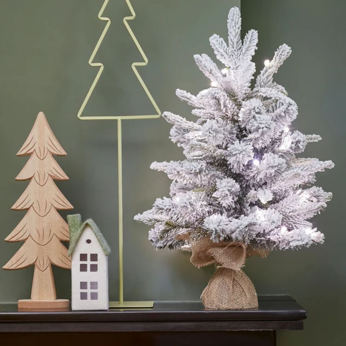A lit artificial snow tree next to wooden and house decorations.