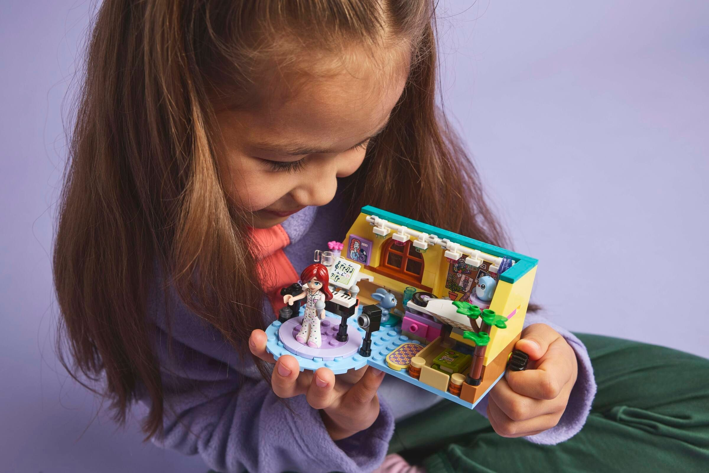 Ein Mädchen hält ein Lego-Modell eines Musikstudios mit einer Figur, einem Klavier und einem Mikrofon.