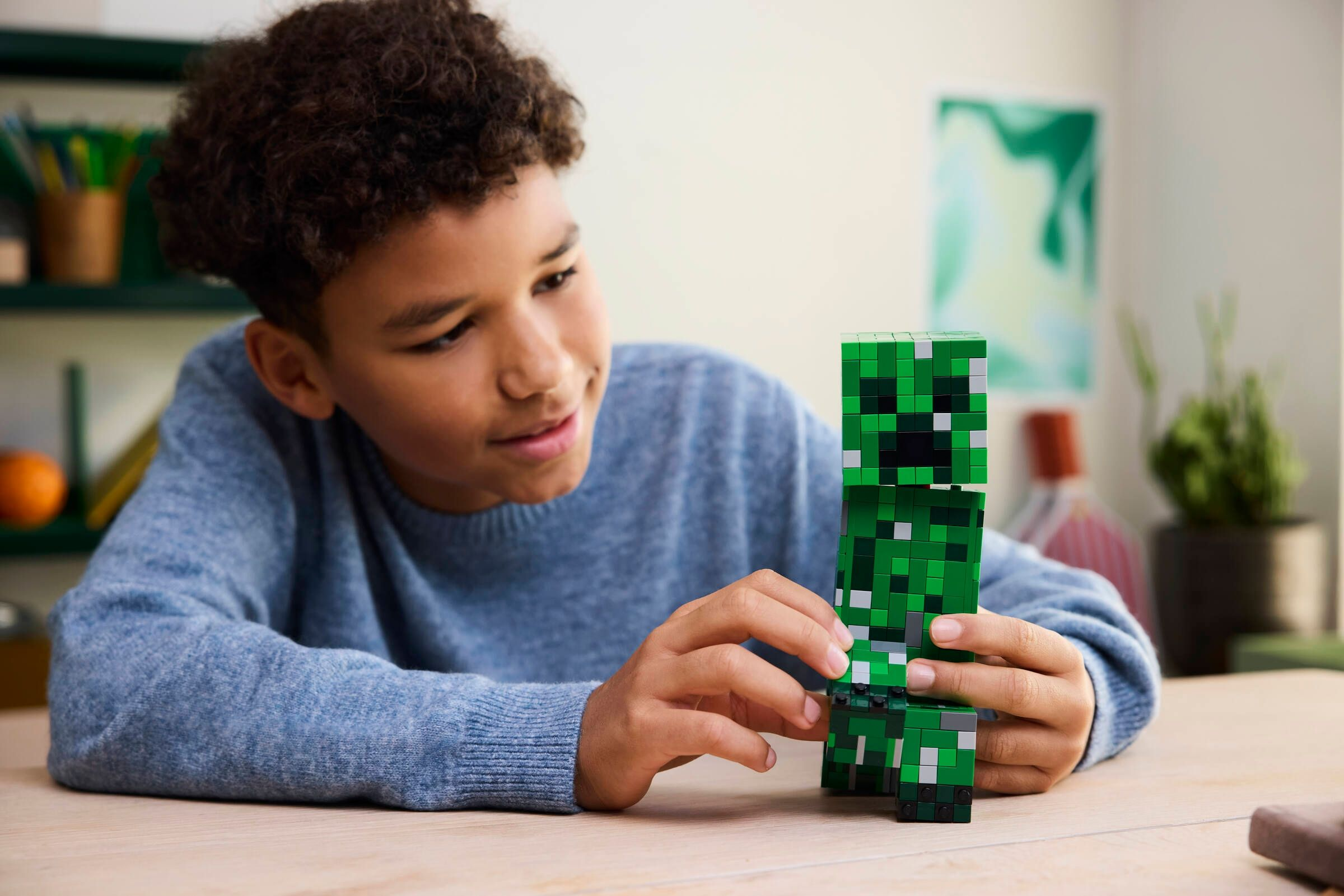 Un ragazzo con i capelli ricci costruisce una figura Minecraft verde con blocchi.