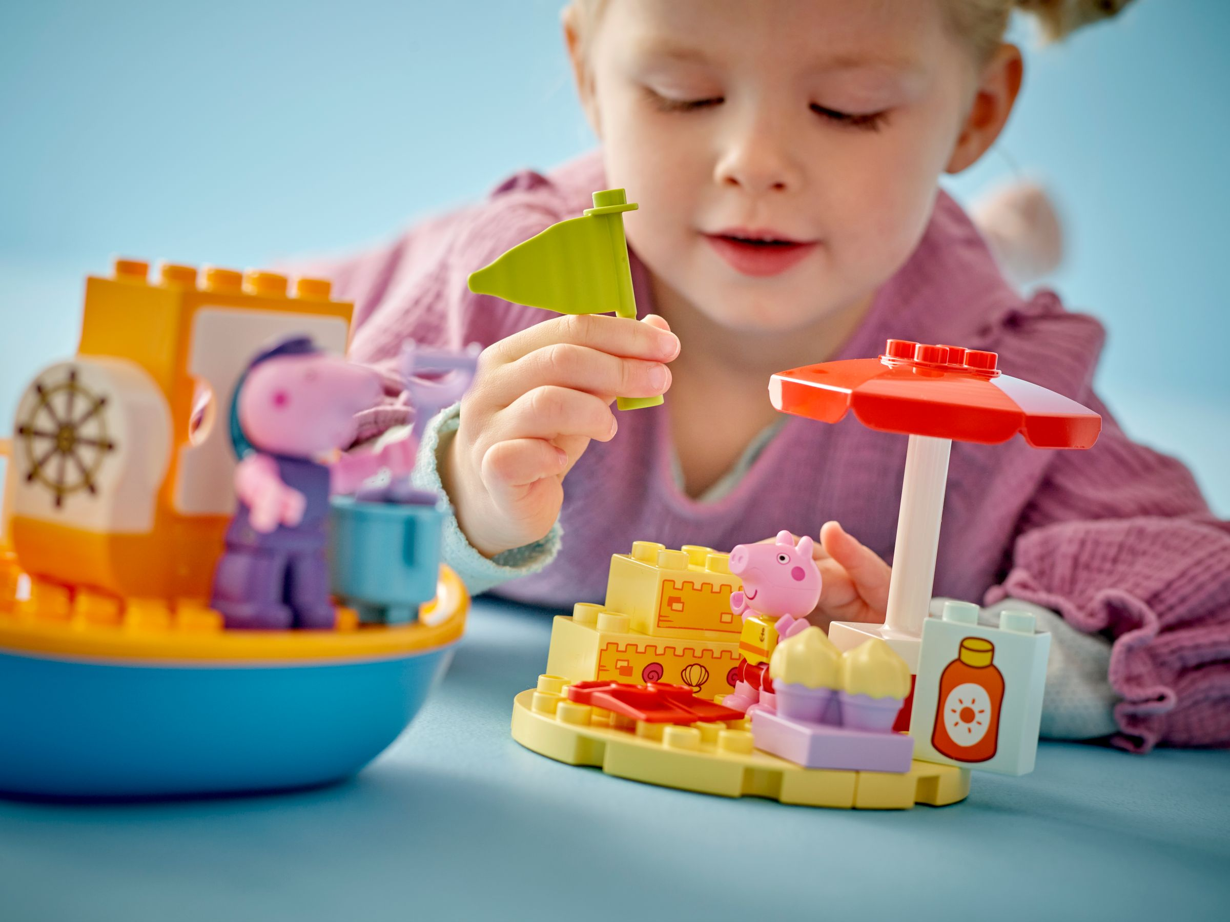Ein kleines Mädchen spielt mit bunten Bausteinen und Figuren auf einem blauen Tisch.