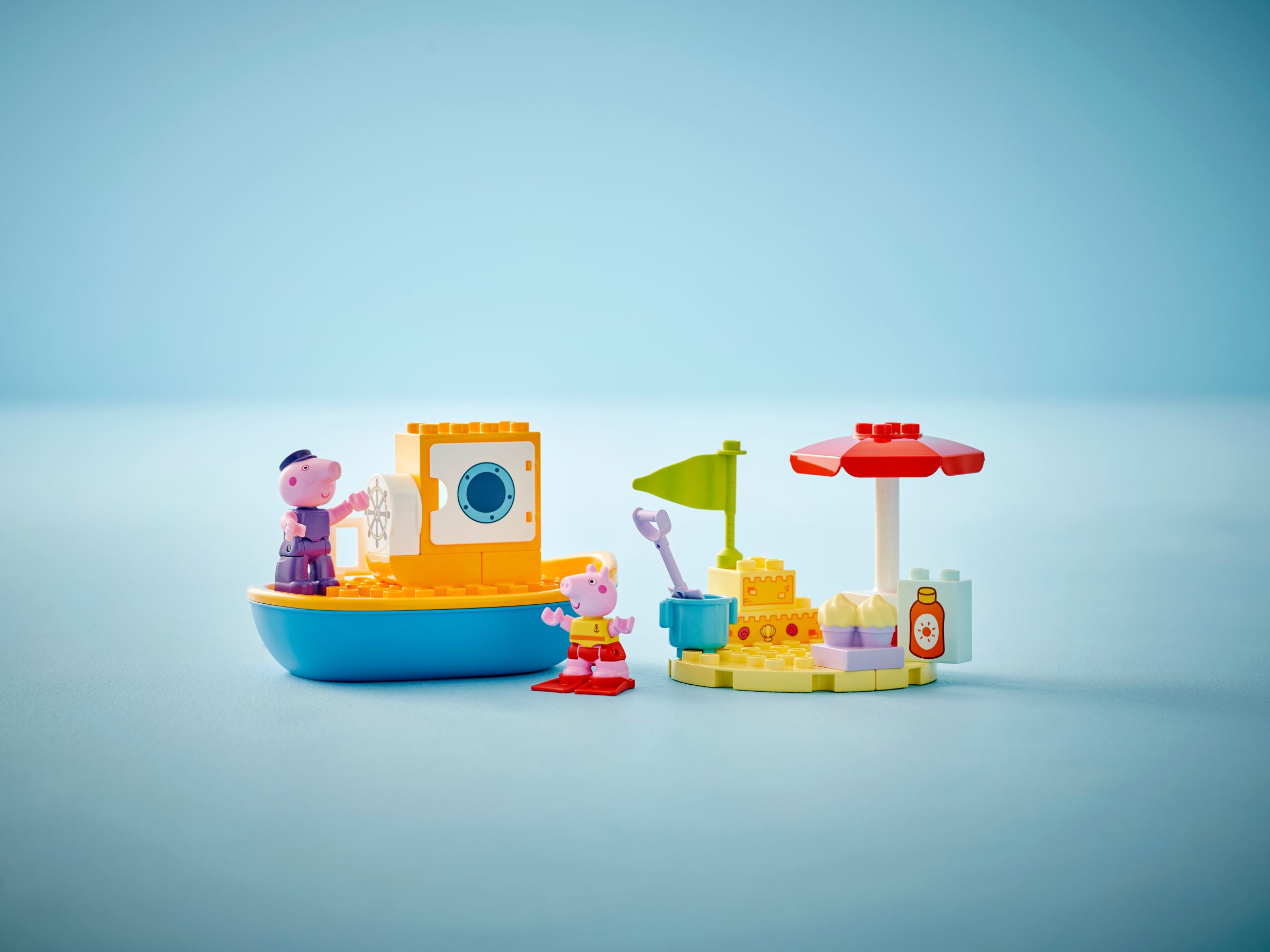 Peppa Wutz und Schorsch auf einem Spielzeugboot und Strand mit Sonnenschirm.