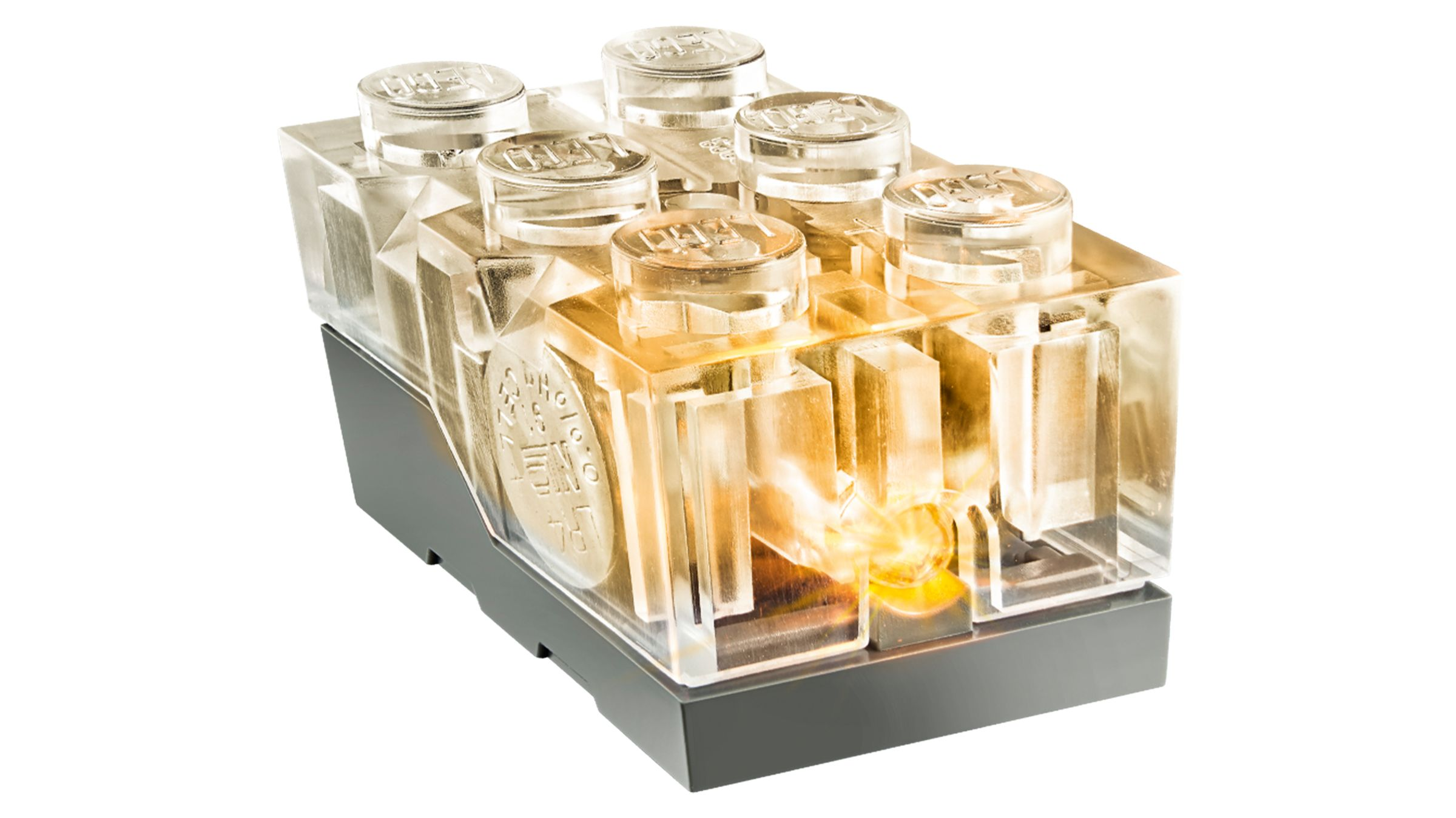 Ein transparenter LEGO-Stein mit goldenen Lichtern im Inneren auf schwarzem Sockel.