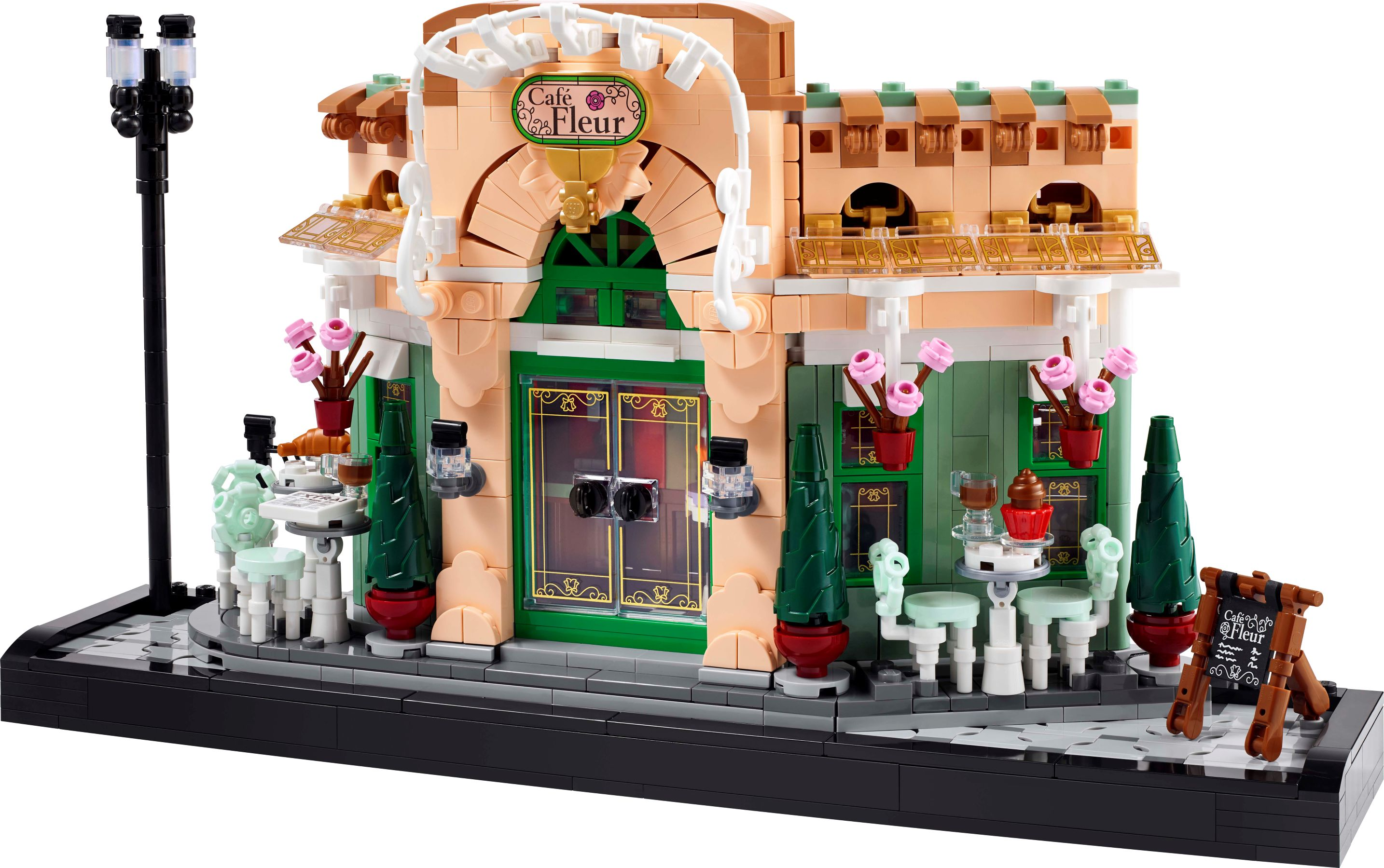 Ein Lego-Café mit grünen Türen, rosa Blumen und Tischen draußen.