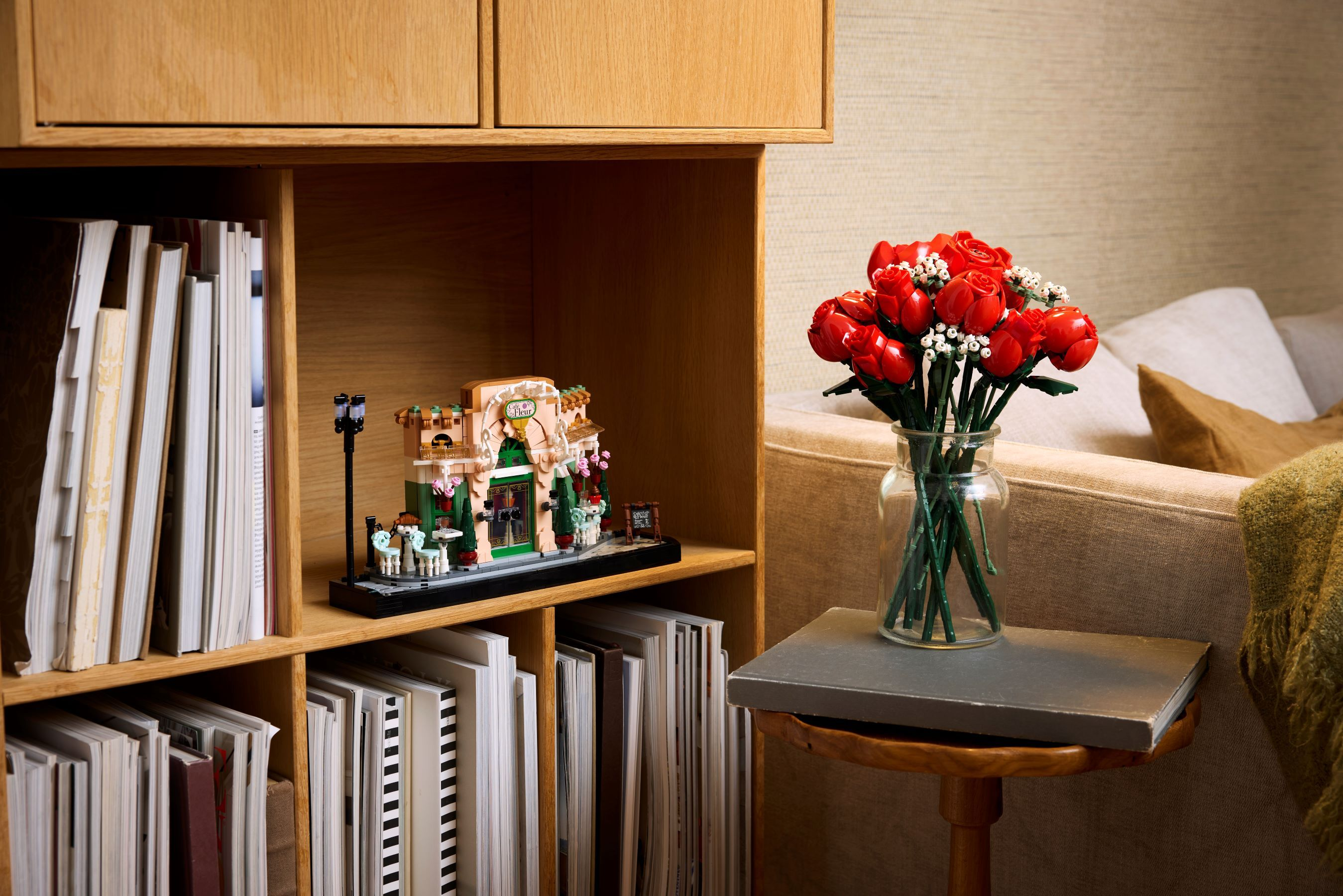 Ein Lego-Blumenladen-Set auf einem Regal neben Büchern und einer Vase mit roten Rosen.