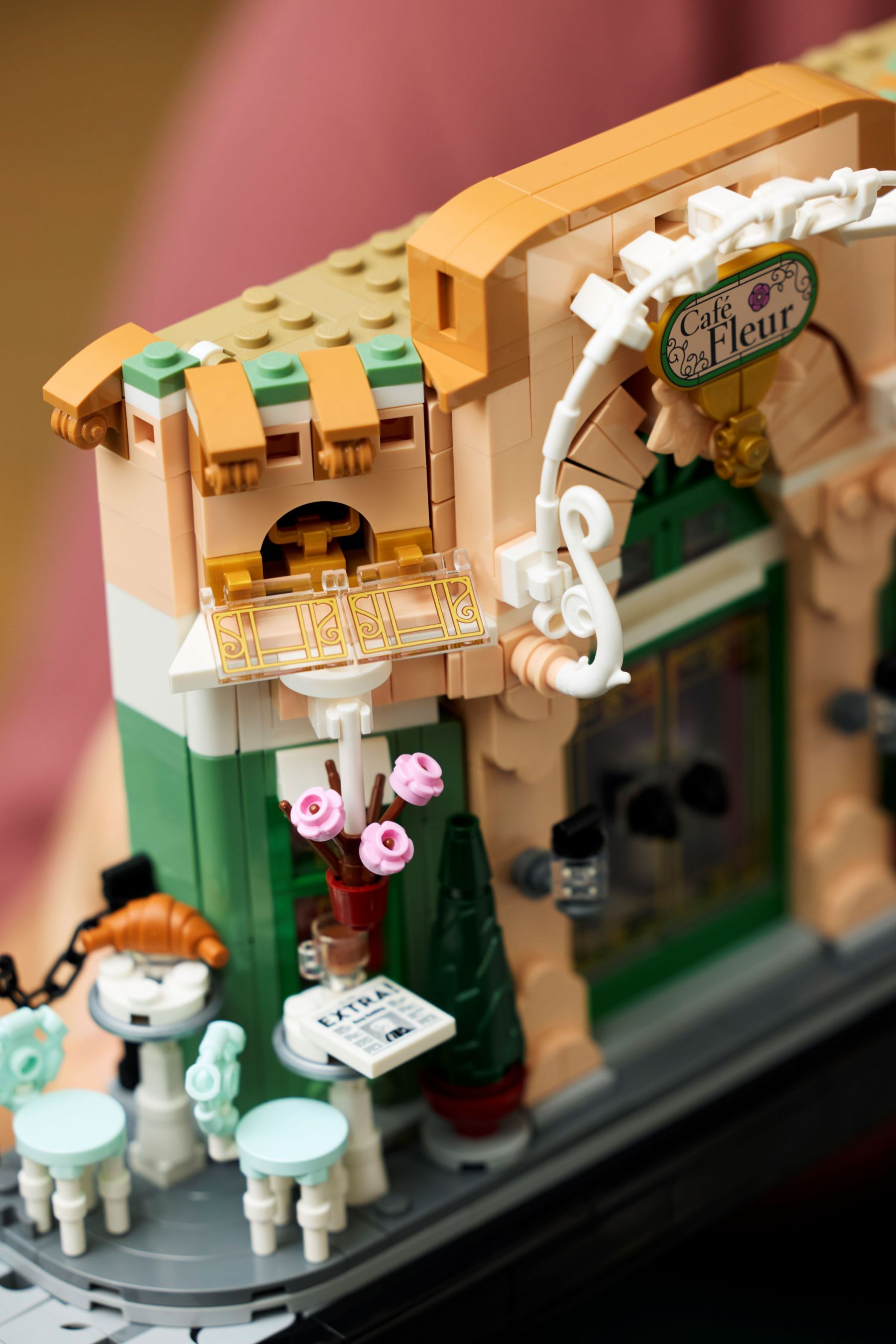 Lego-Nachbau eines Cafés mit Tischen, Stühlen, einem Croissant und Blumen.
