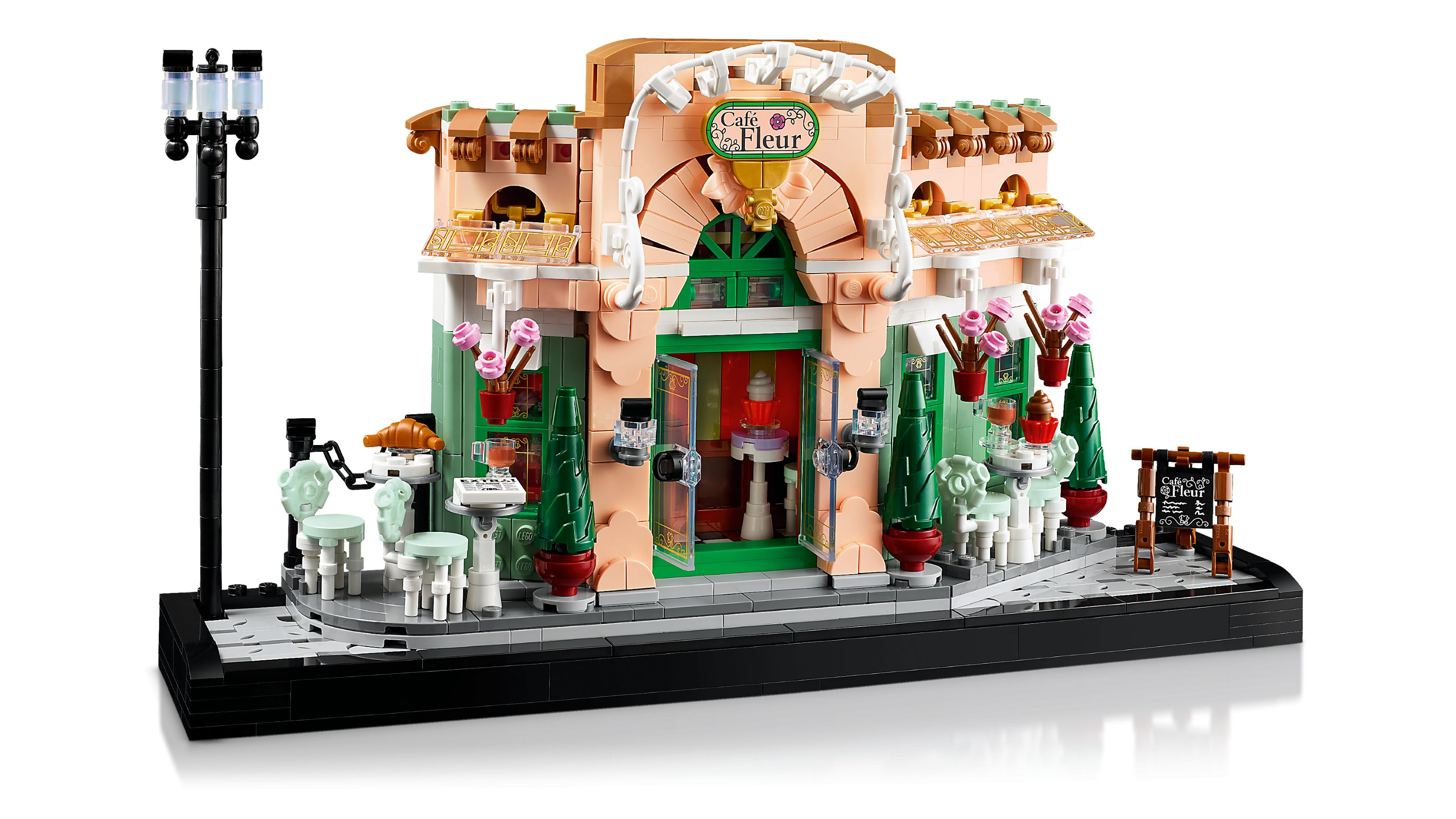 Ein Lego-Café mit rosa Fassade, grünen Akzenten und Außensitzplätzen.