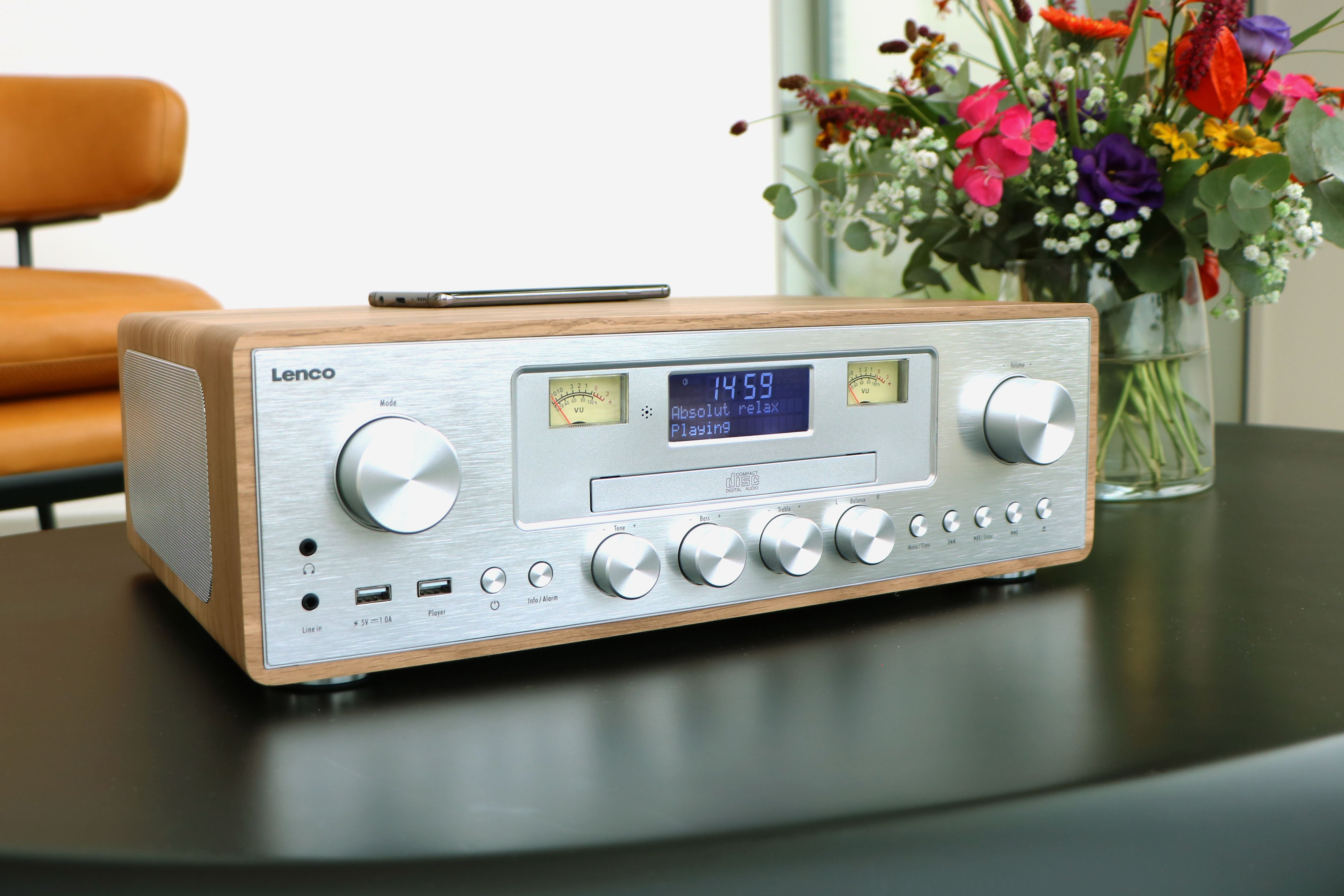 Een Lenco radio met houten behuizing staat op een tafel, met bloemen ernaast.