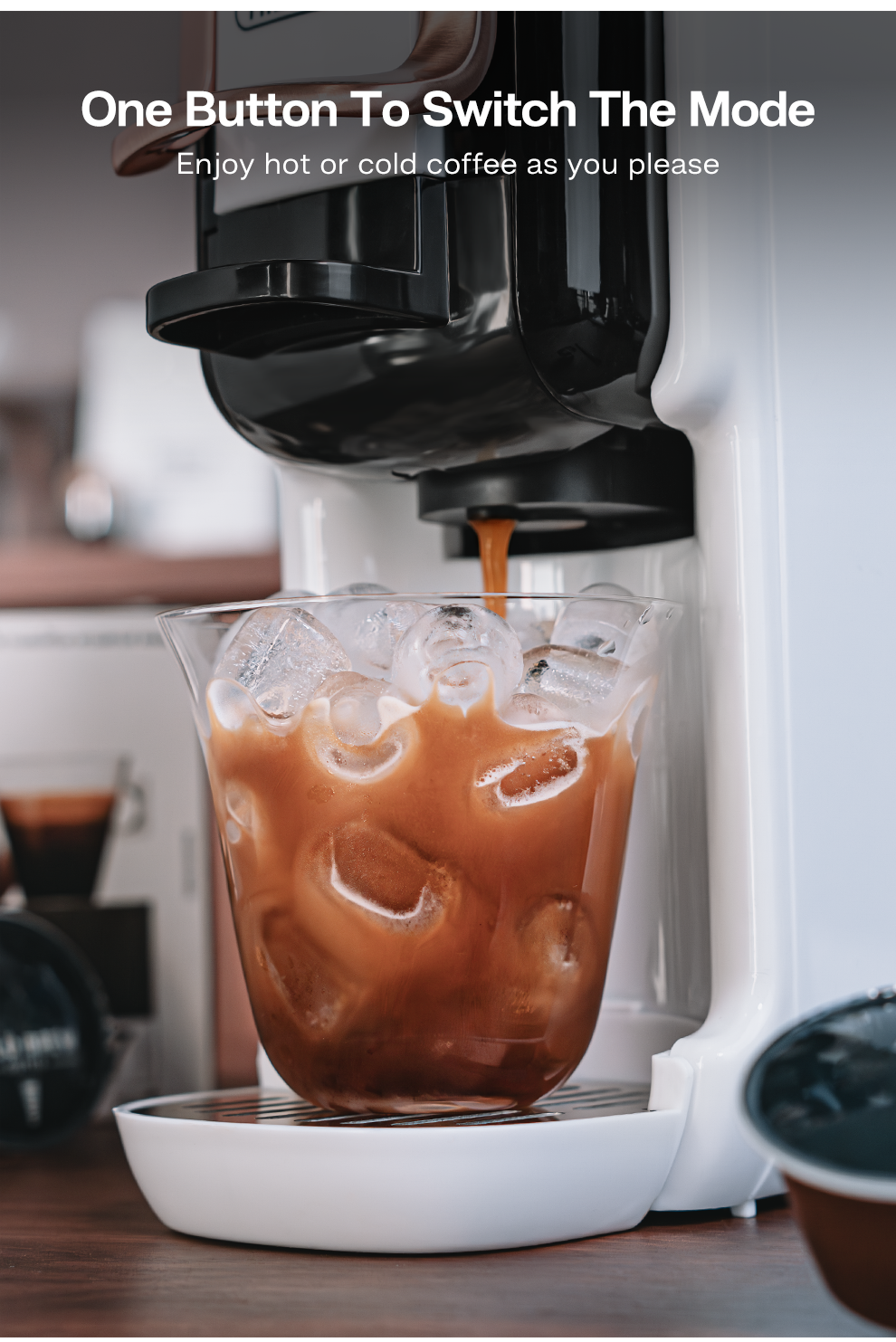 Café helado vertiéndose en un vaso con cubitos de hielo. Cafetera al fondo.