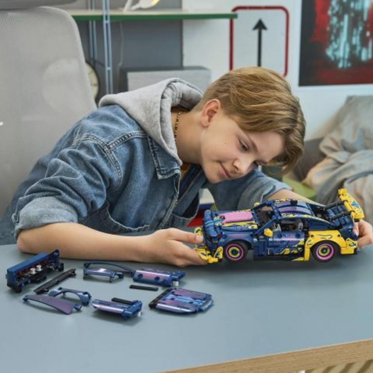 Un ragazzo costruisce un'auto Lego blu e gialla. Diverse parti sono accanto.