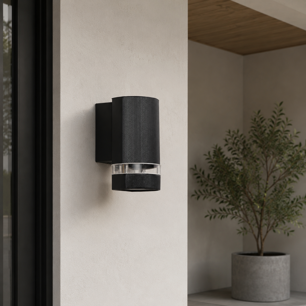 Lámpara de pared exterior negra con detalle acanalado y vidrio transparente, junto a ventana y planta.