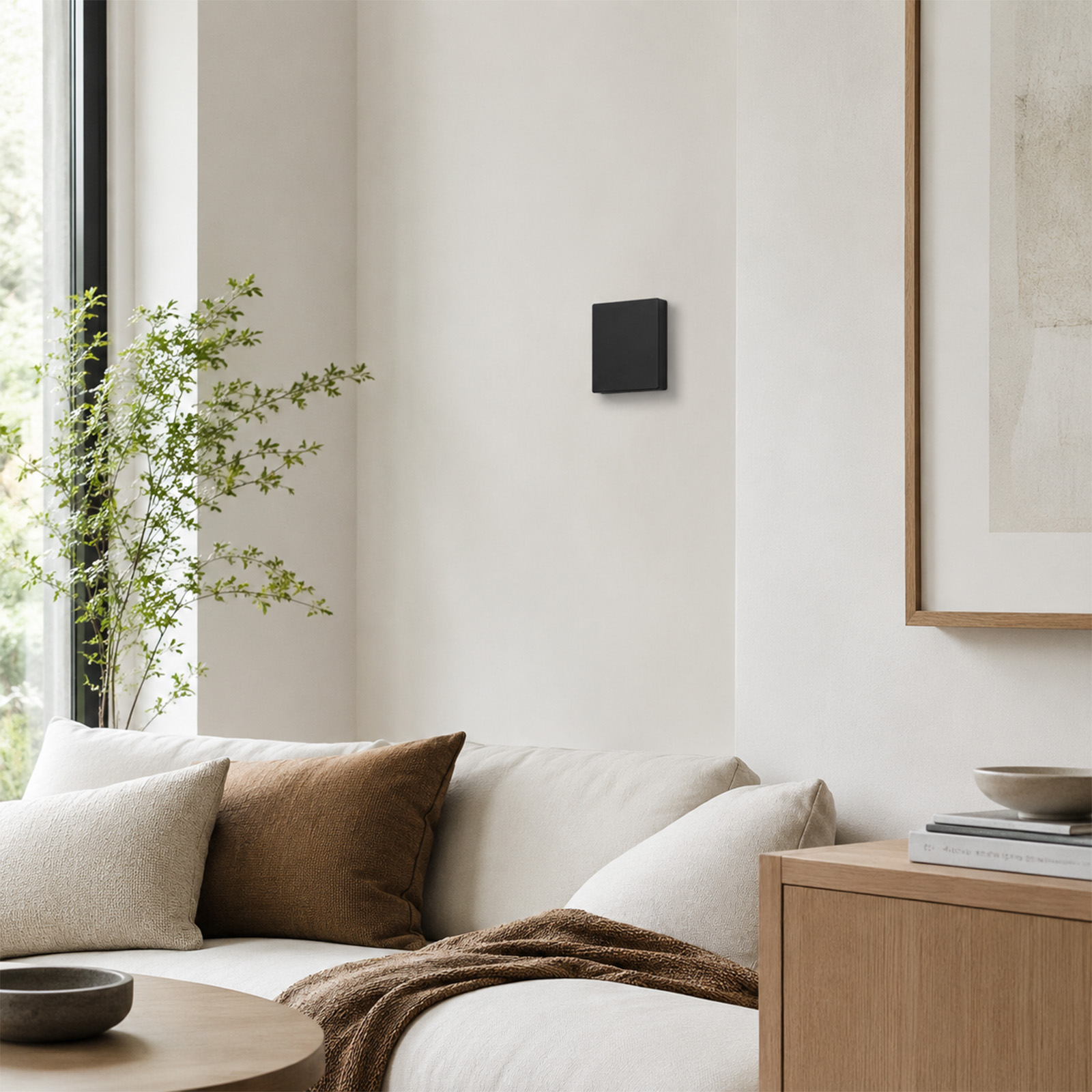 Una sala con sofá, cojines, manta, mesa y un cuadrado negro en la pared.