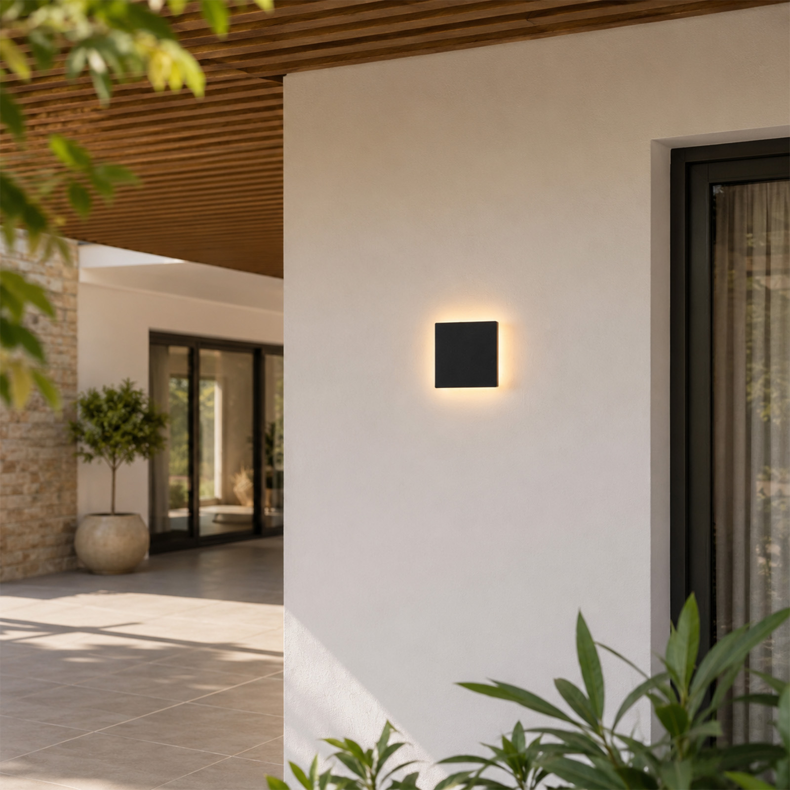 Aplique de pared negro ilumina pared blanca sobre terraza con plantas.