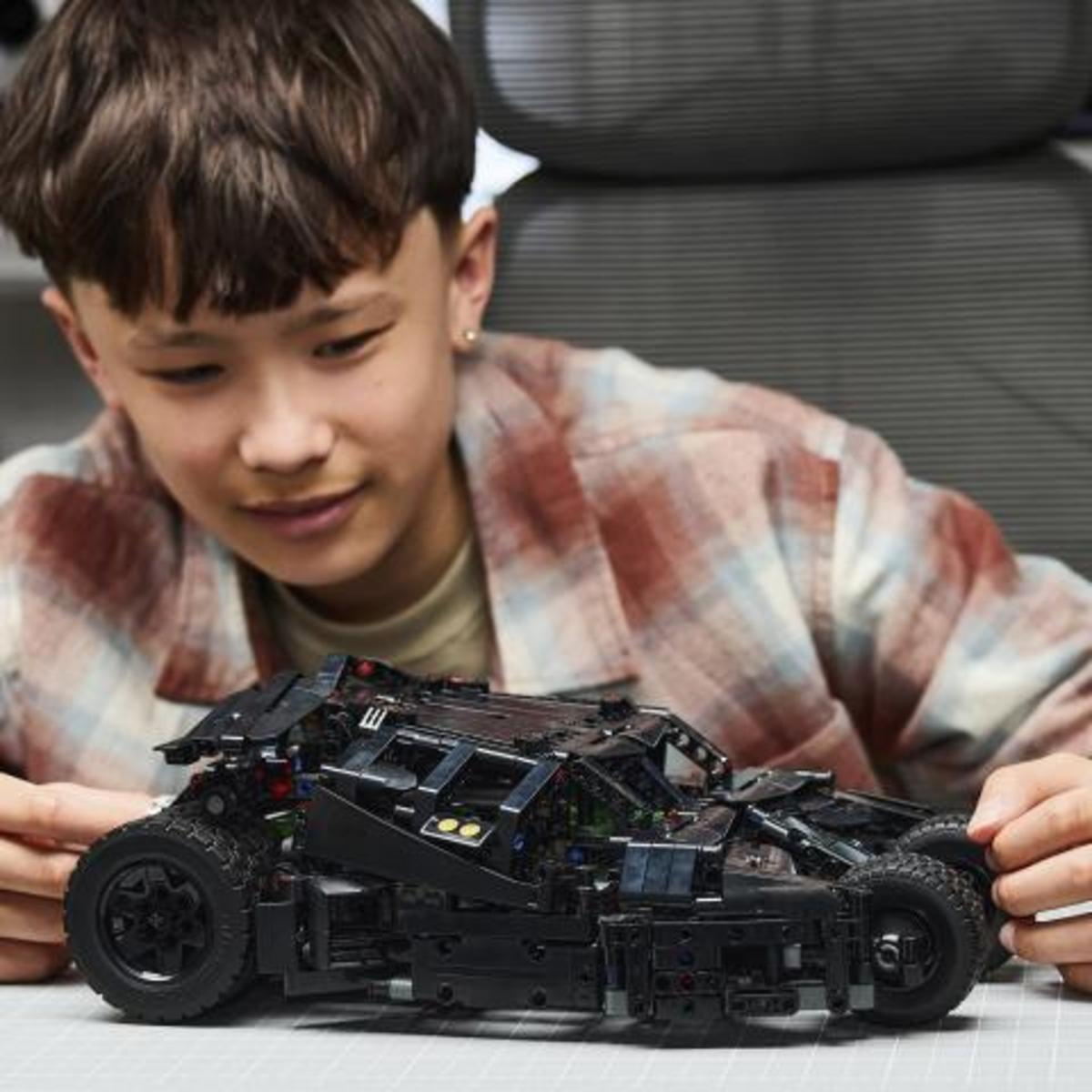 Ragazzo con camicia a quadri costruisce Batmobile Lego nera con dettagli.