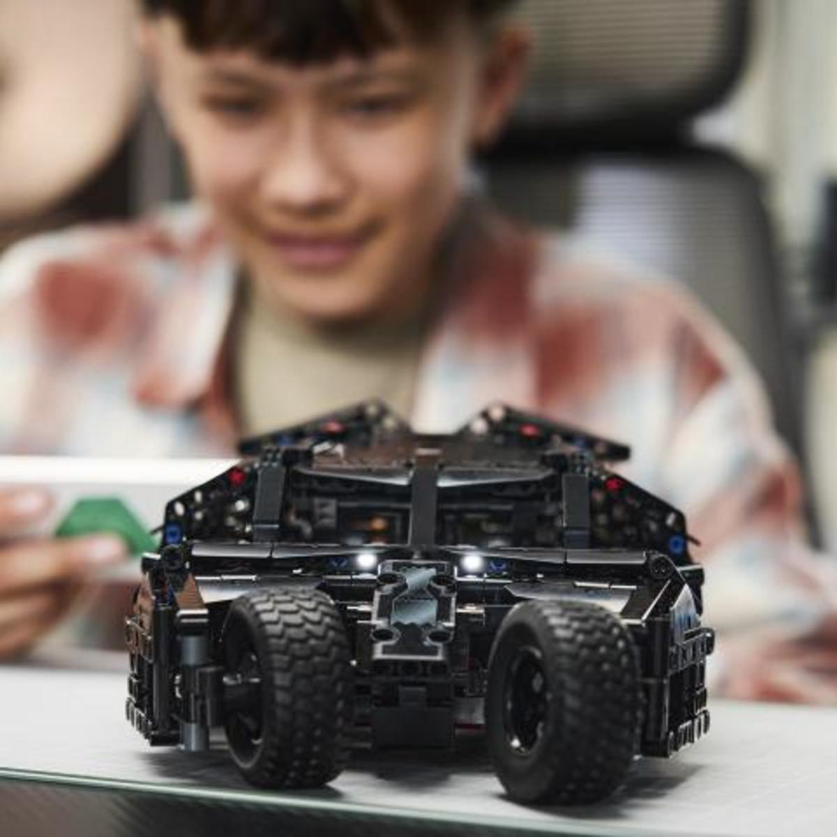 Un ragazzo guarda una Batmobile Lego nera con ruote grandi.