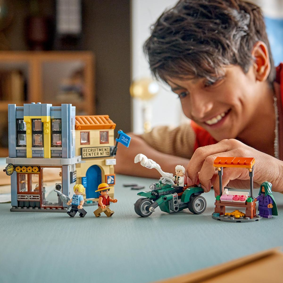 Ragazzo costruisce set Lego con moto, figure ed edifici a un tavolo.