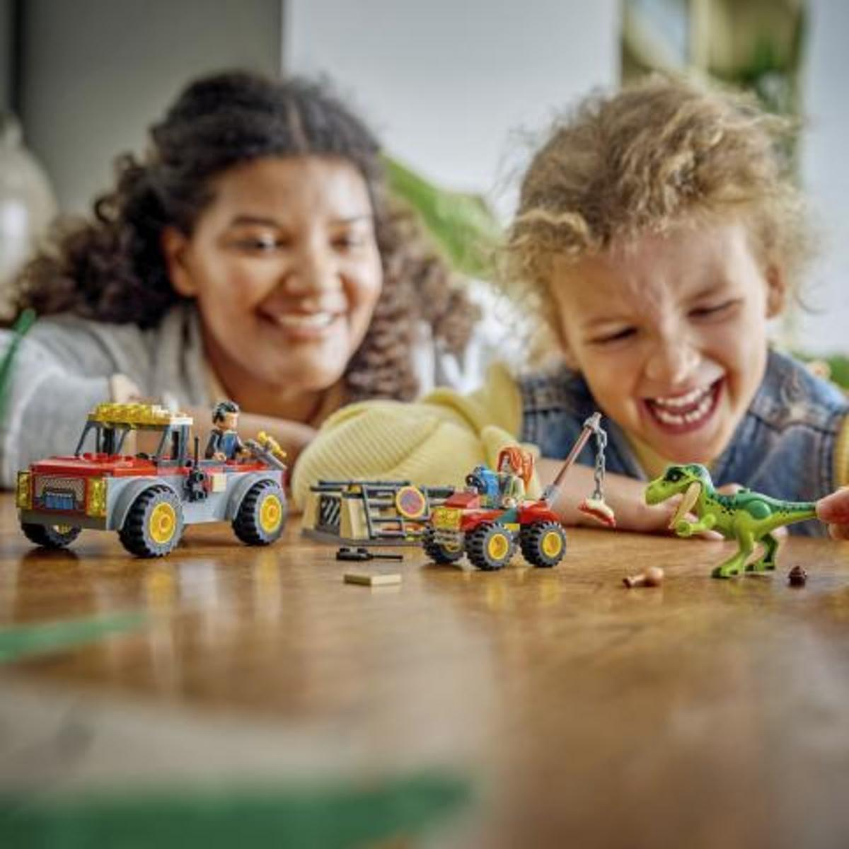 Bambini giocano con veicoli giocattolo di dinosauri e una figura di dinosauro verde.