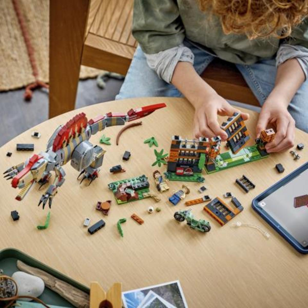 Un bambino costruisce un dinosauro Lego e un set di Jurassic Park su un tavolo di legno.