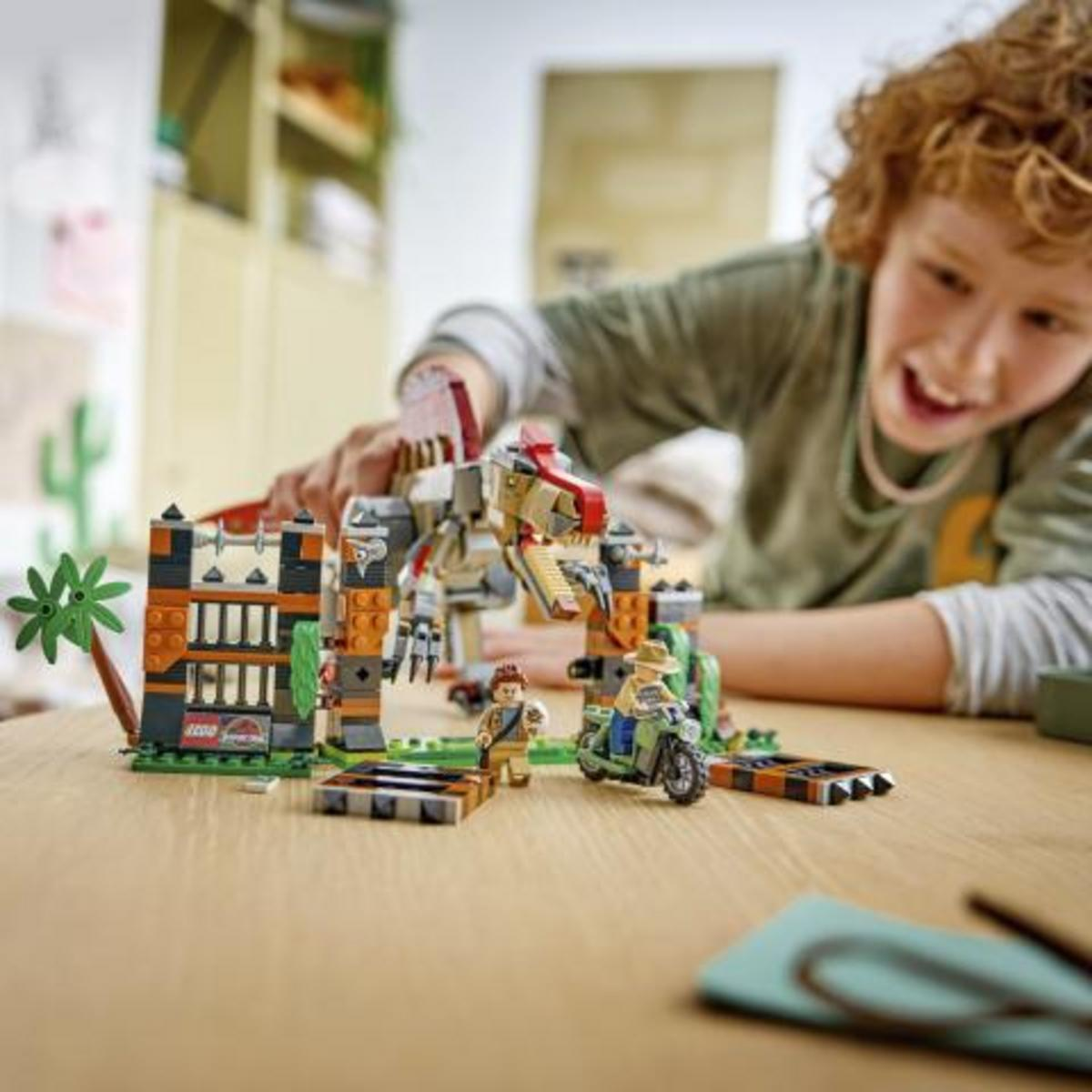 Un ragazzo gioca con un set di dinosauri Lego su un tavolo di legno.