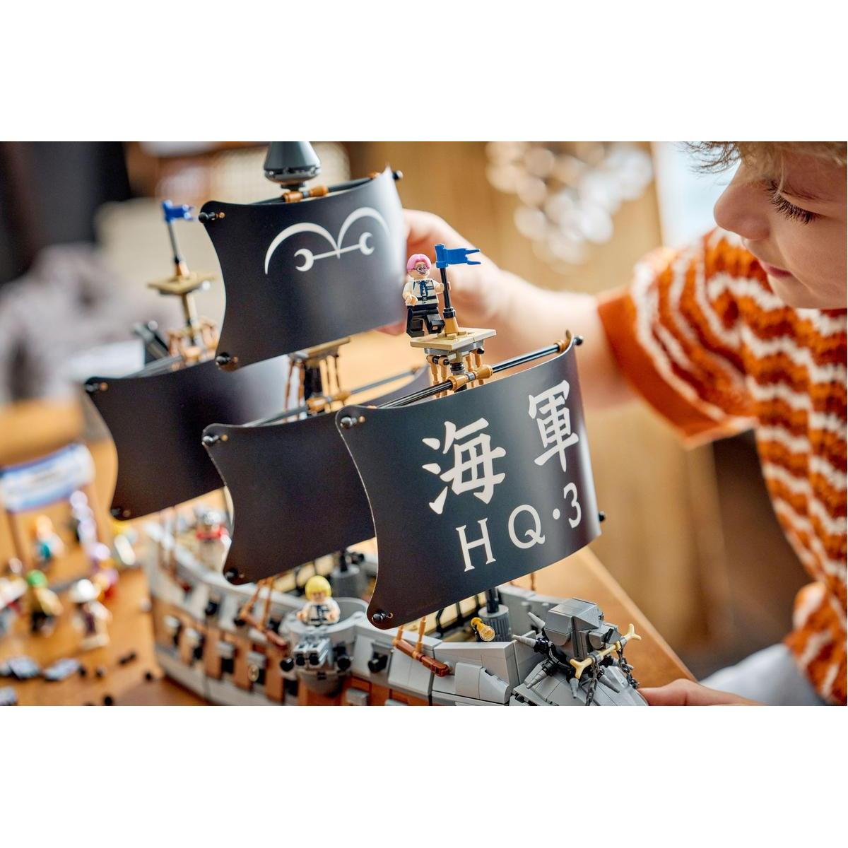 Un niño construye un barco pirata Lego con velas negras y texto japonés.