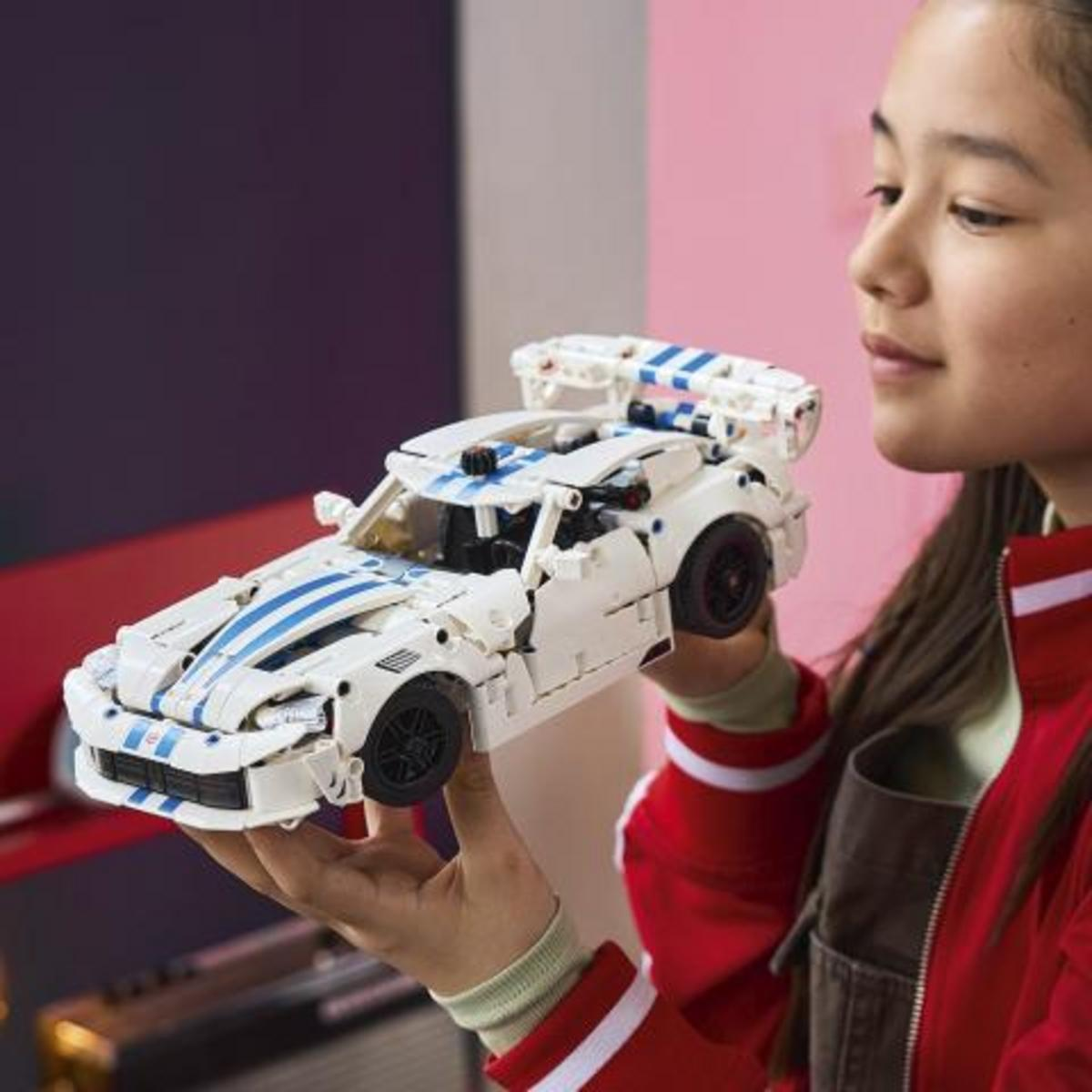 Kız, mavi çizgili ve spoylerli beyaz bir Lego araba tutuyor.