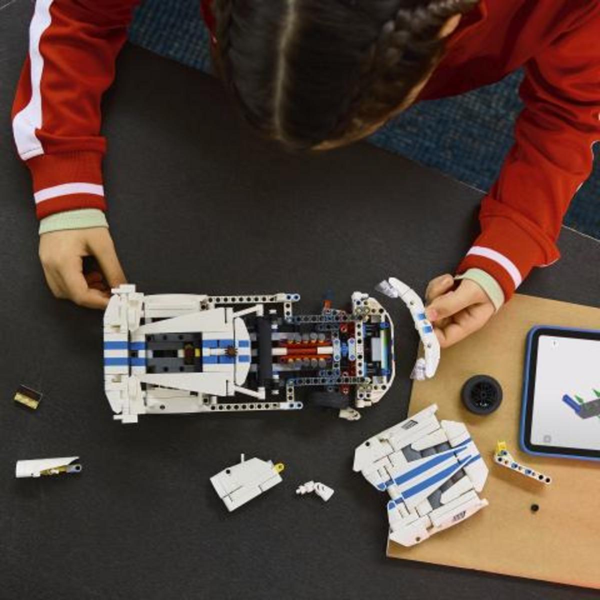 Çocuk, tablet üzerindeki talimatlarla beyaz ve mavi Lego araba yapıyor.