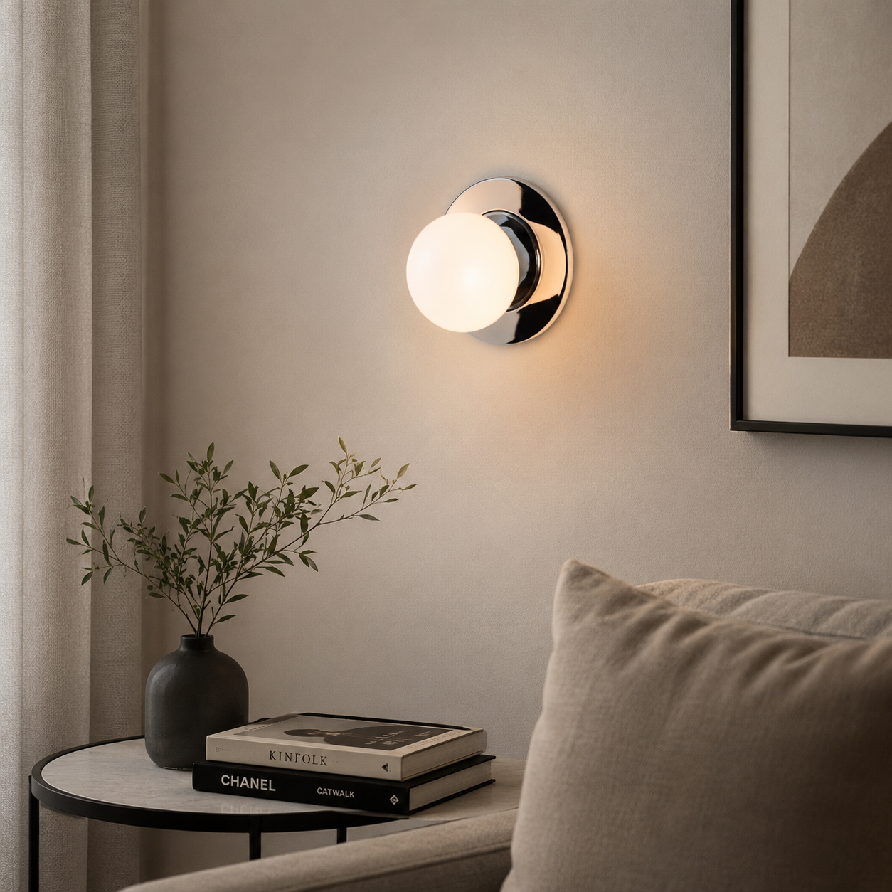 Lámpara de pared con cristal esmerilado y cromo, junto a una mesa con libros y jarrón.