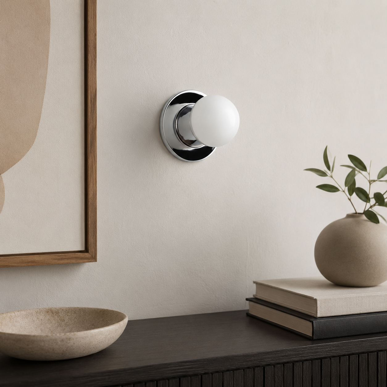 Una lámpara de pared con base plateada y globo blanco sobre una pared.