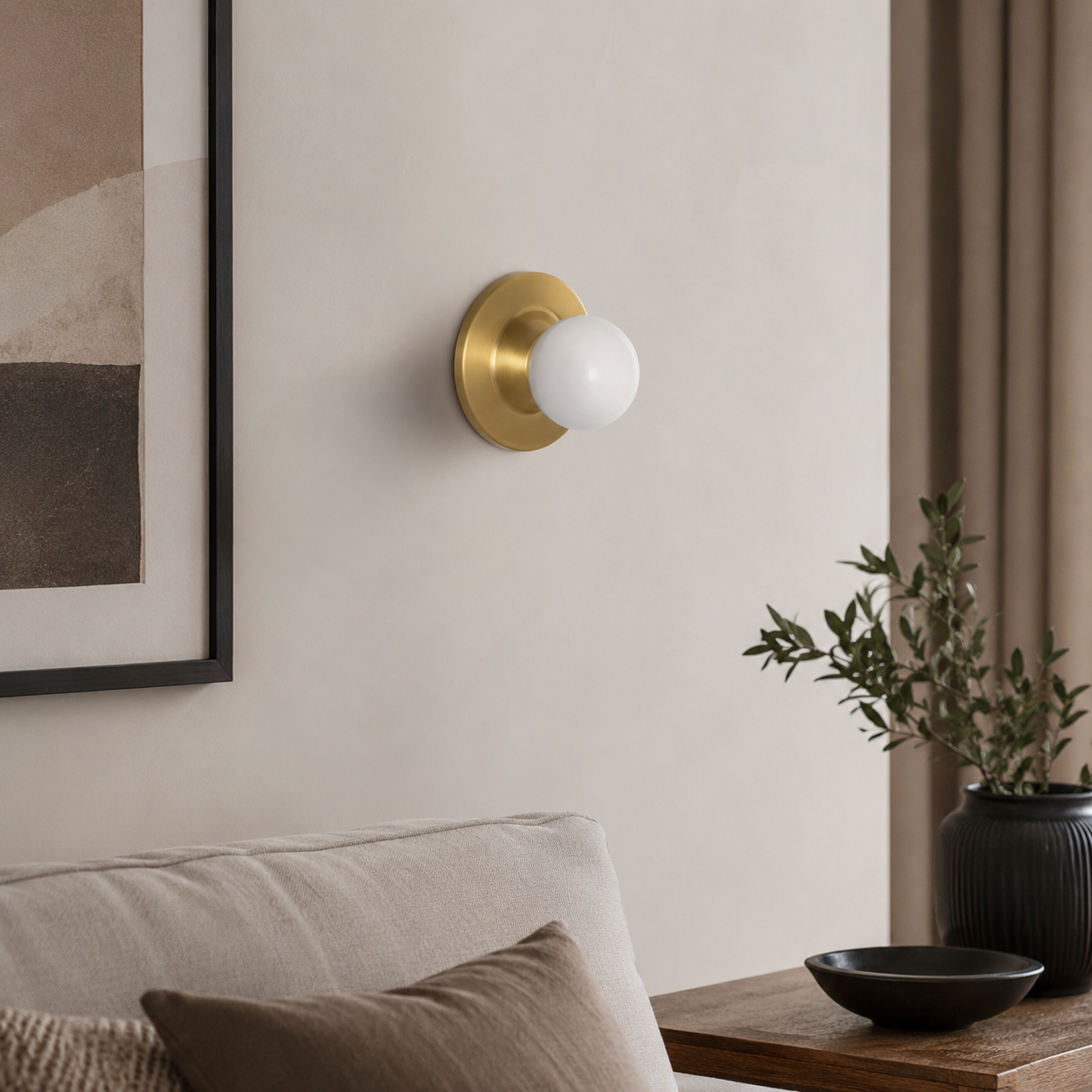 Aplique de pared dorado con bombilla blanca, junto a sofá y obra de arte.