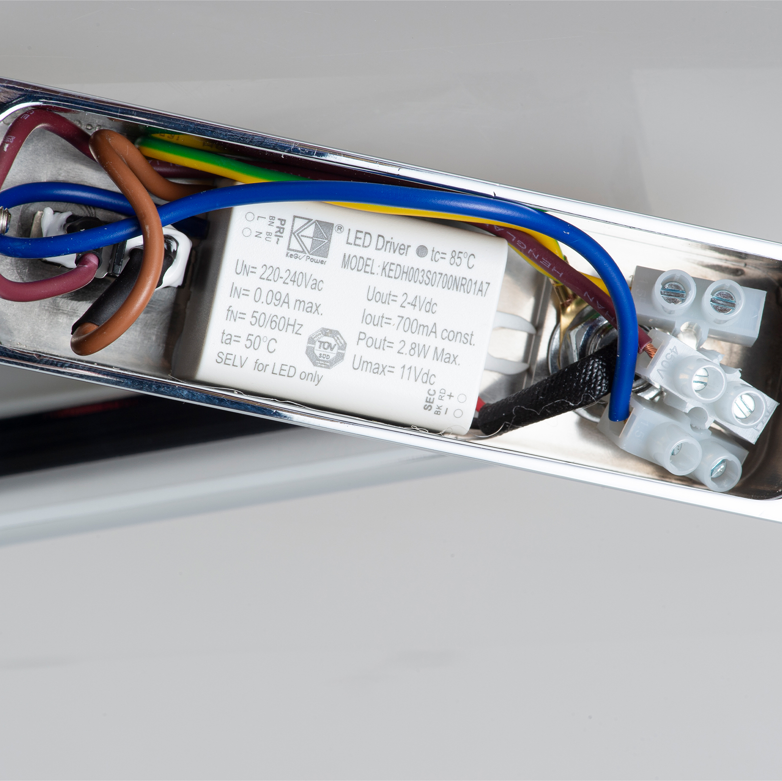 Un controlador LED blanco con cables y conectores dentro de una carcasa cromada.