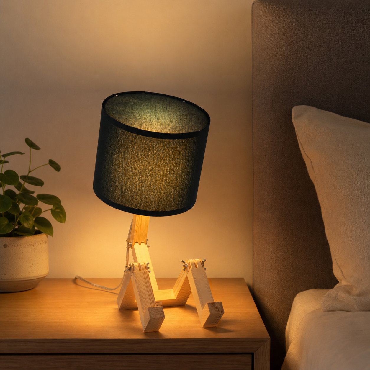 Una peculiar lámpara robot de madera se sienta en una mesita de noche junto a una cama y una planta en maceta.