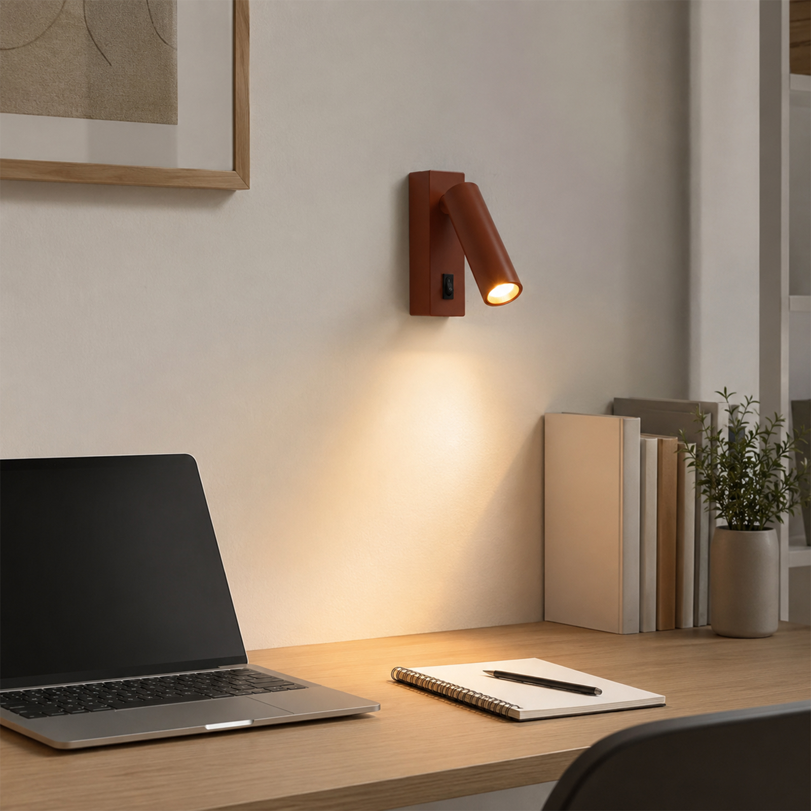 Una luz de pared marrón ilumina un escritorio con portátil, cuaderno y libros.