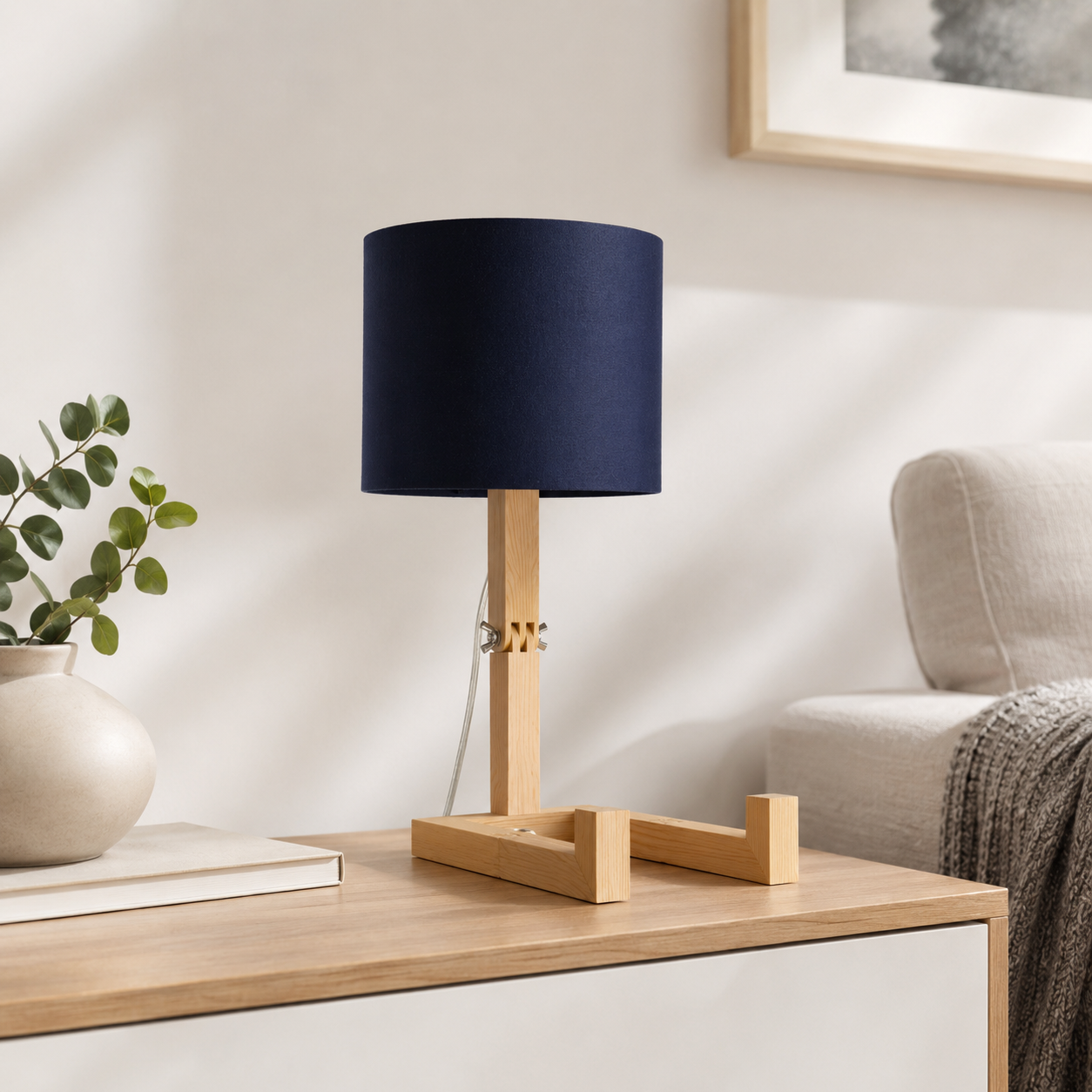 Lámpara de madera con pantalla azul marino junto a un jarrón con plantas.