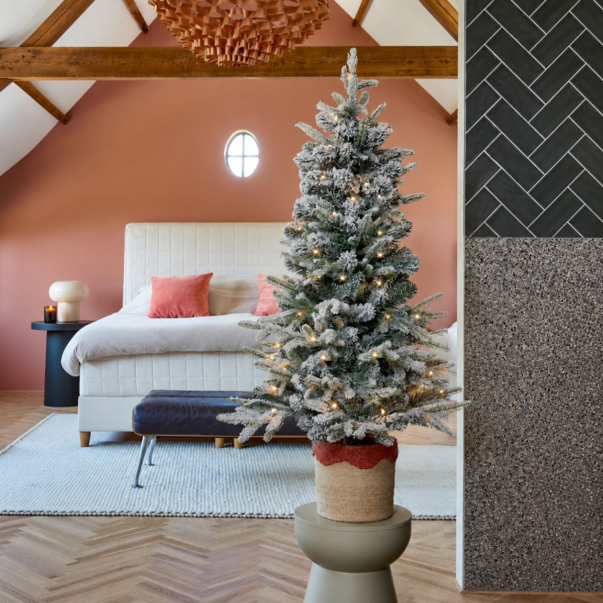 A decorated Christmas tree stands in a bedroom next to a bed with linens.