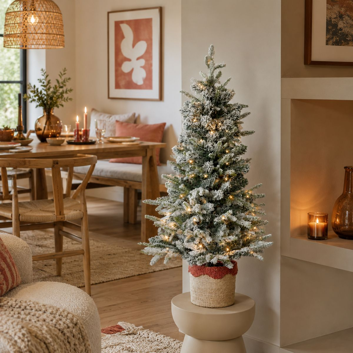 A flocked artificial Christmas tree with lights sits on a stool in a dining room.