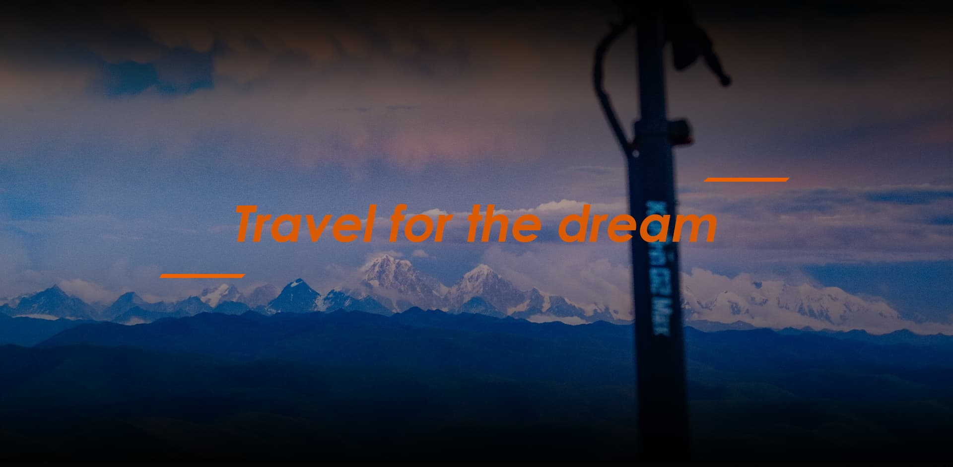 Il manubrio di uno scooter si erge davanti a una catena montuosa con nuvole. Testo: Travel for the dream.