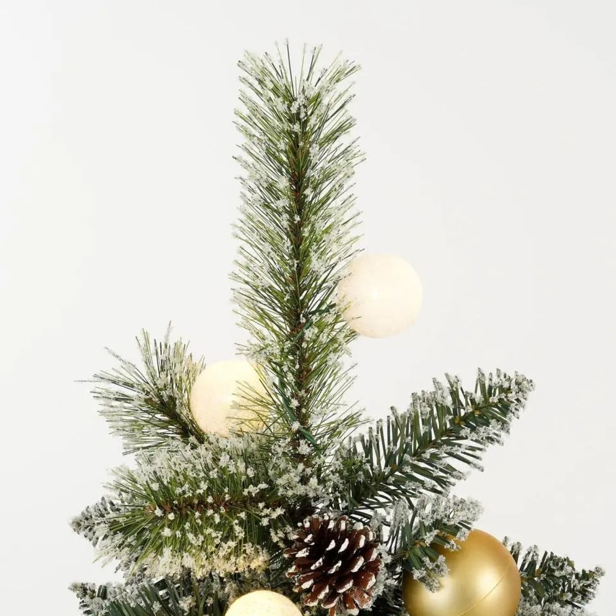 Close-up van een besneeuwde kerstboom met dennenappels en gouden en witte kerstballen.