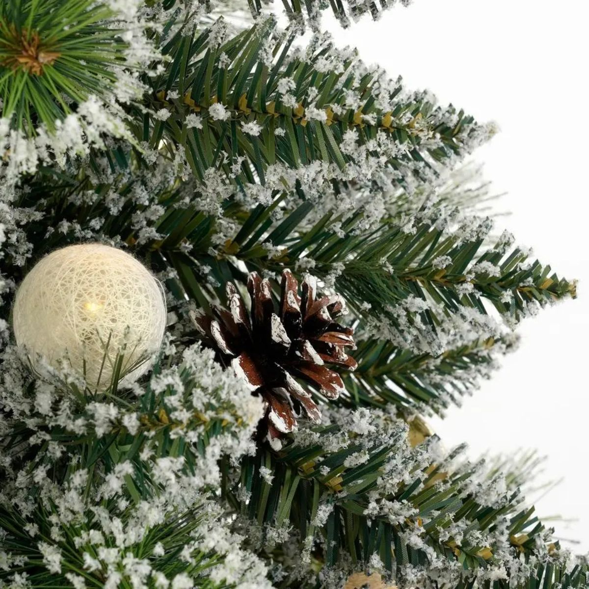 Close-up van een besneeuwde dennentak met een dennenappel en een witte lantaarn.