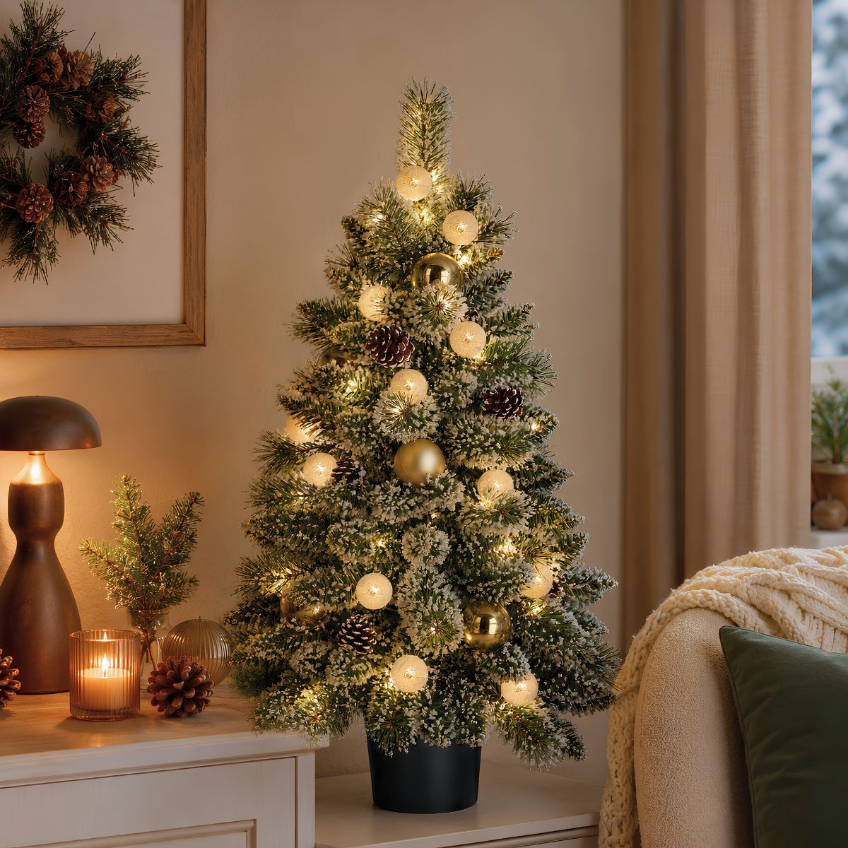 Een versierde kerstboom met lampjes en ornamenten staat op een dressoir.