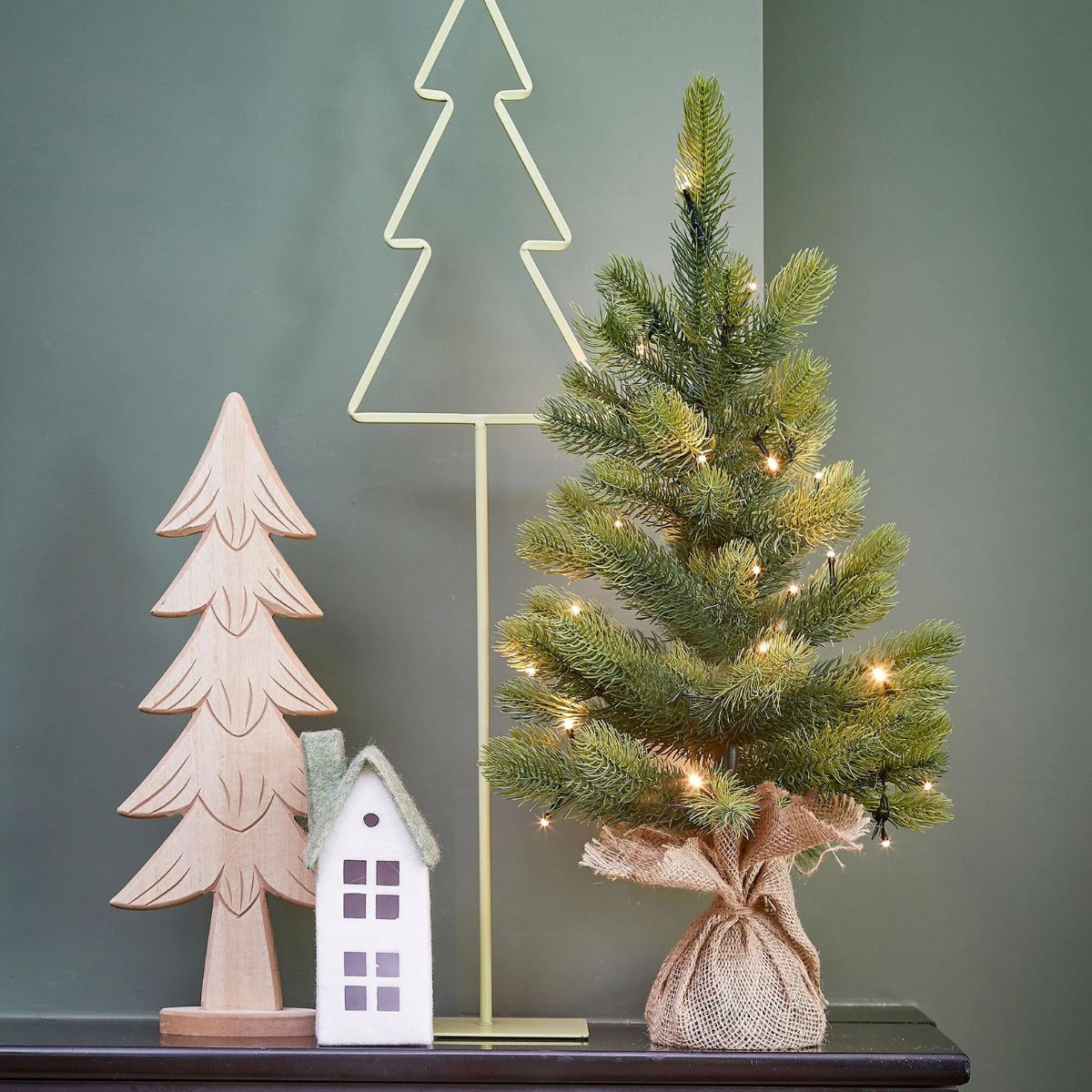 A small Christmas tree with lights sits beside wood and house decorations.