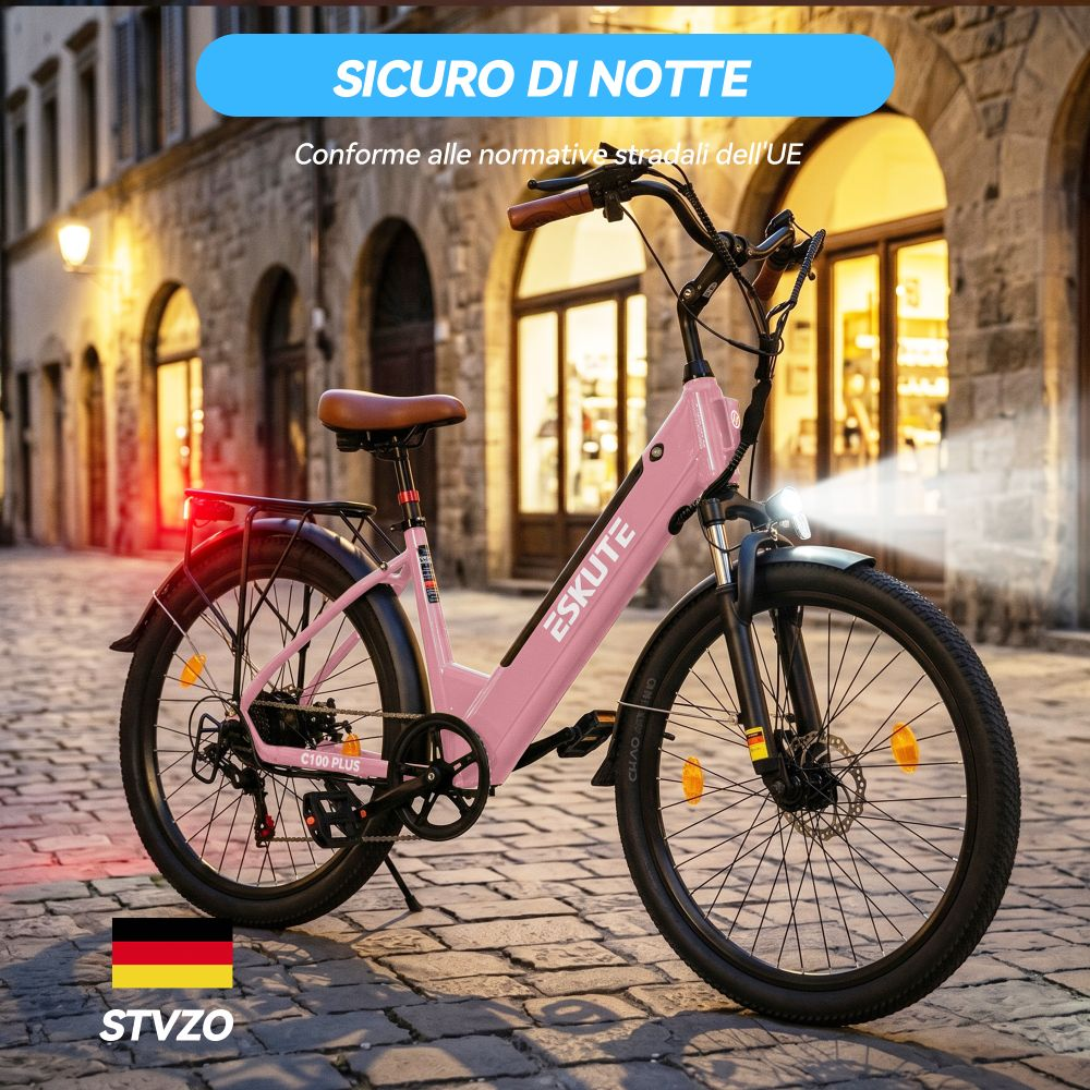 Una e-bike rosa con luci è parcheggiata su una strada acciottolata con edifici sullo sfondo.