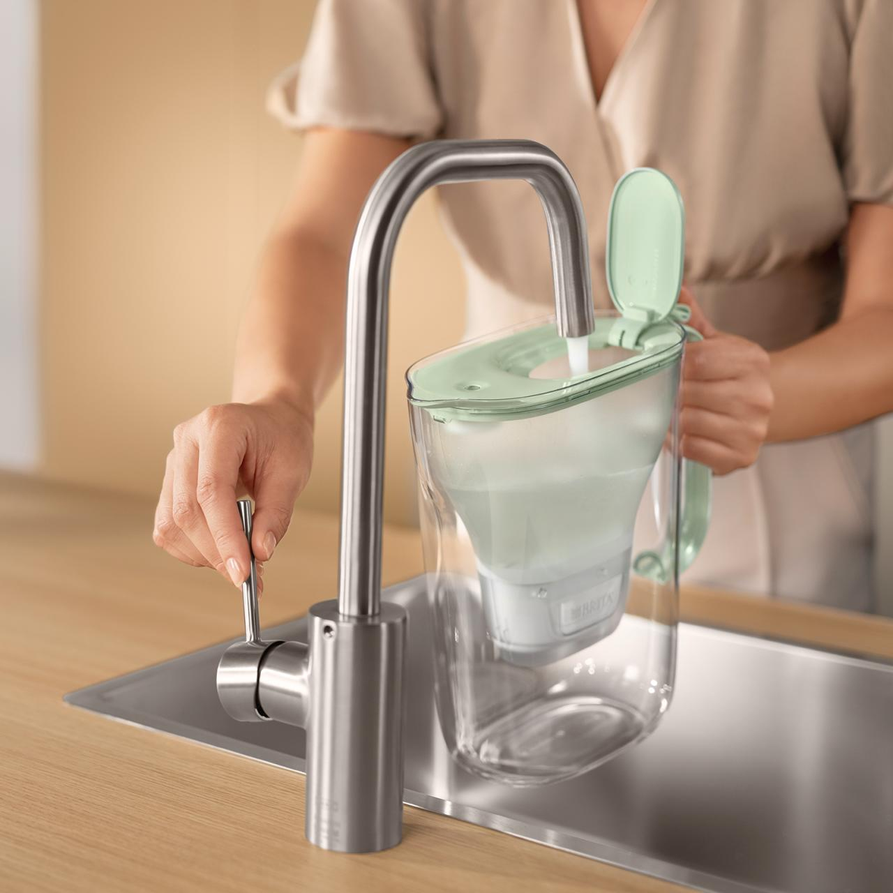Una persona riempie una caraffa filtrante sotto un rubinetto in cucina.