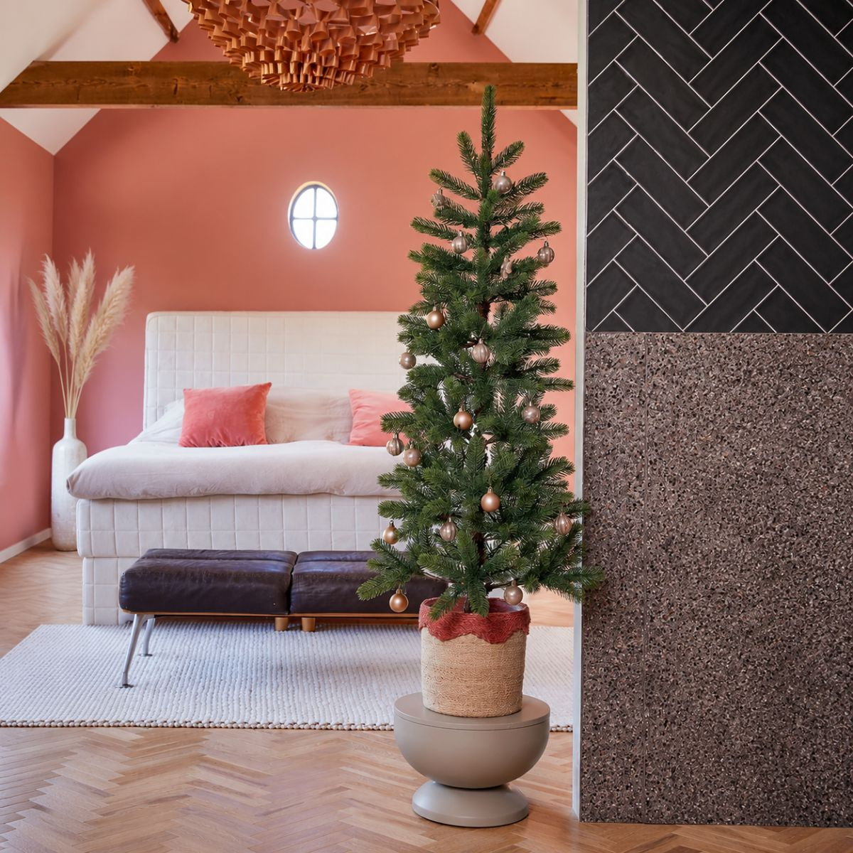 A small Christmas tree with baubles stands beside a bed with salmon pillows.