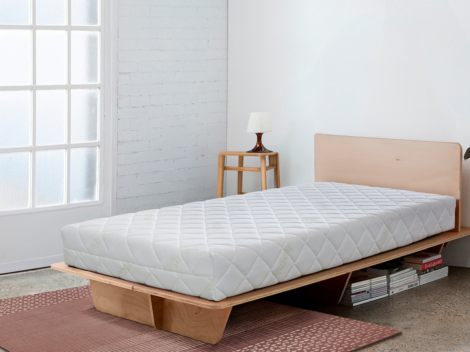 Un colchón blanco sobre una estructura de cama de madera, con una mesita de noche al lado.