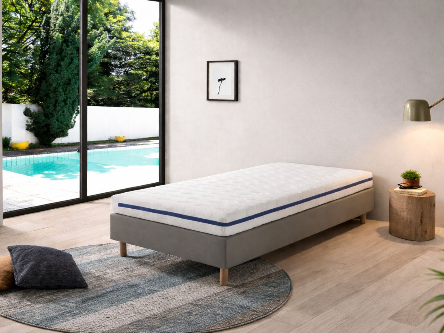 Una cama individual con colchón blanco y rayas azules sobre una alfombra redonda.