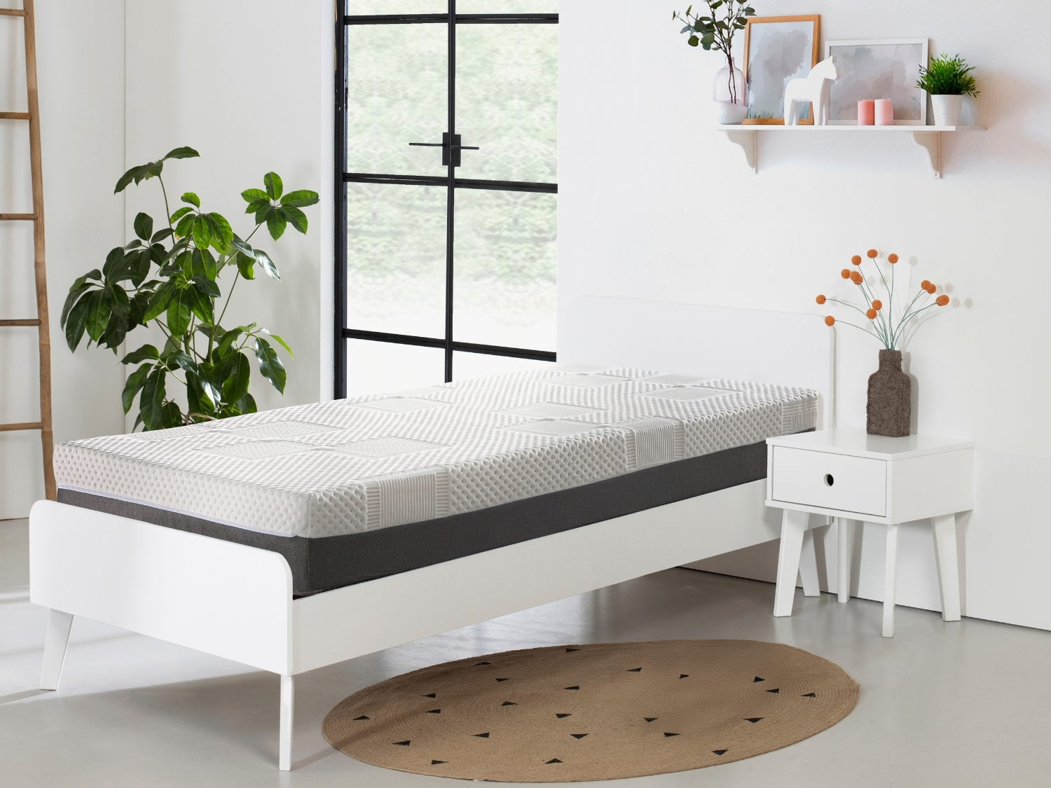 Una cama blanca con colchón, mesita de noche, planta y decoración.