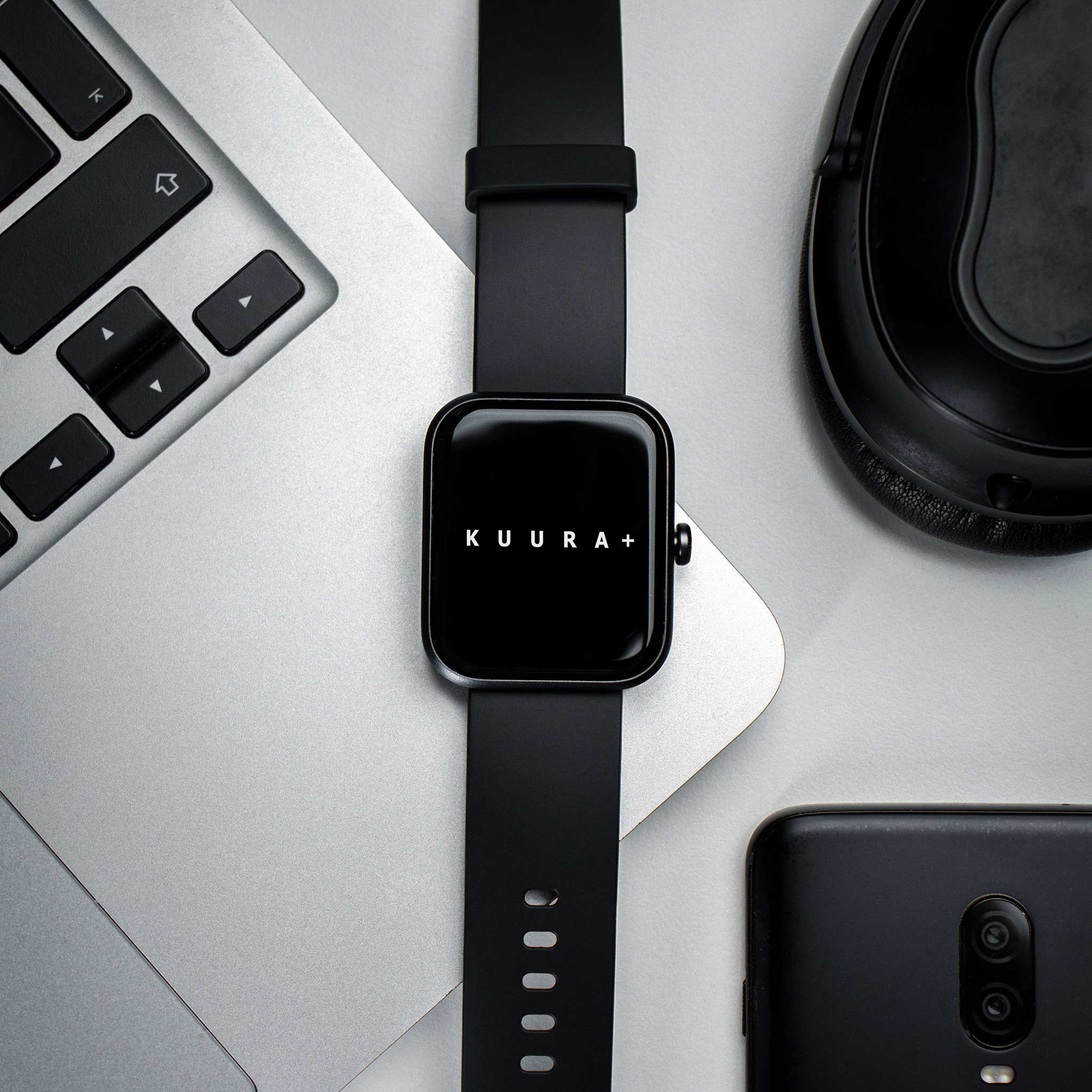 Ein schwarzes Smartwatch mit dem Logo KUU RA+ auf einem Laptop mit Kopfhörern.