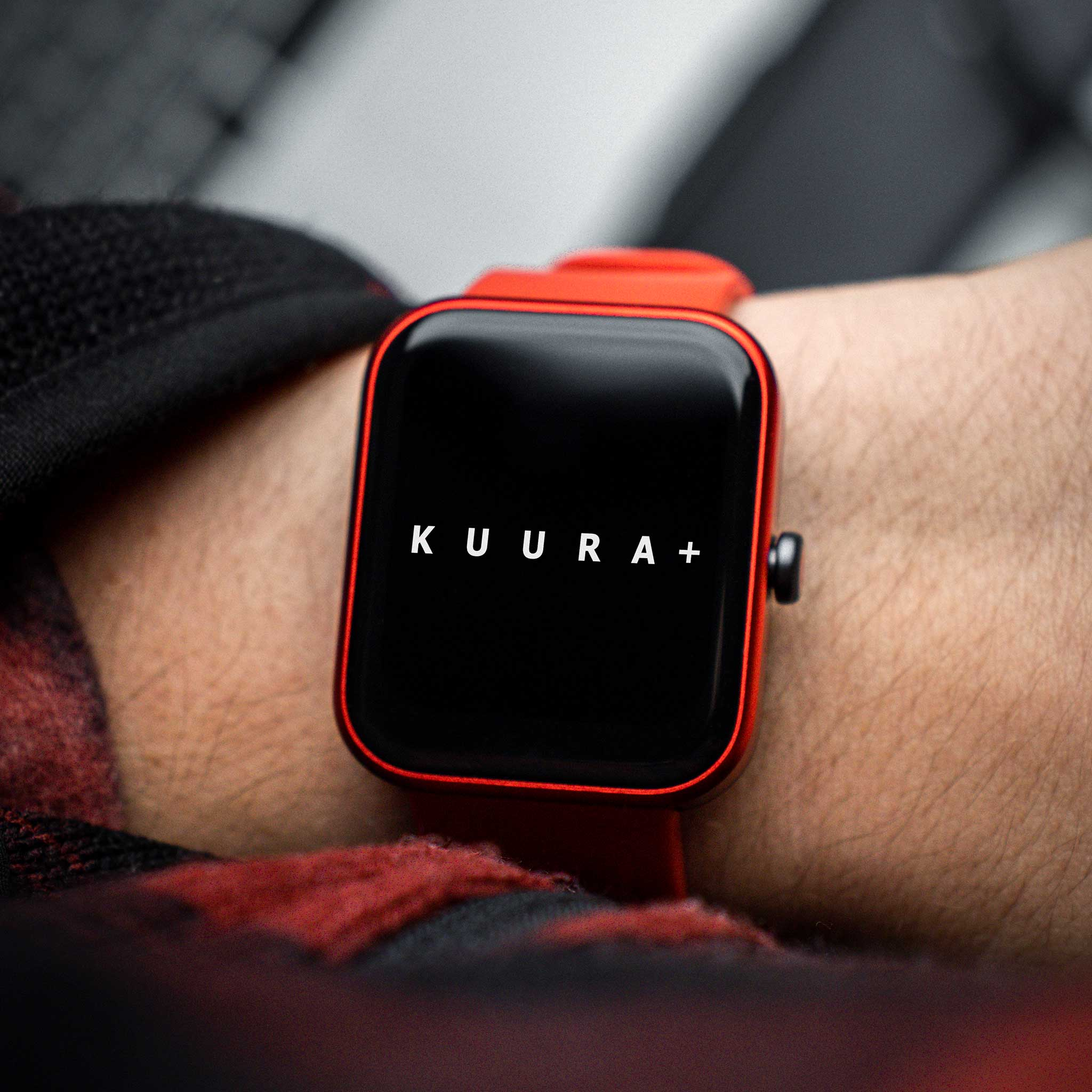 Eine rote Smartwatch mit schwarzem Display, auf dem KUURA+ steht.